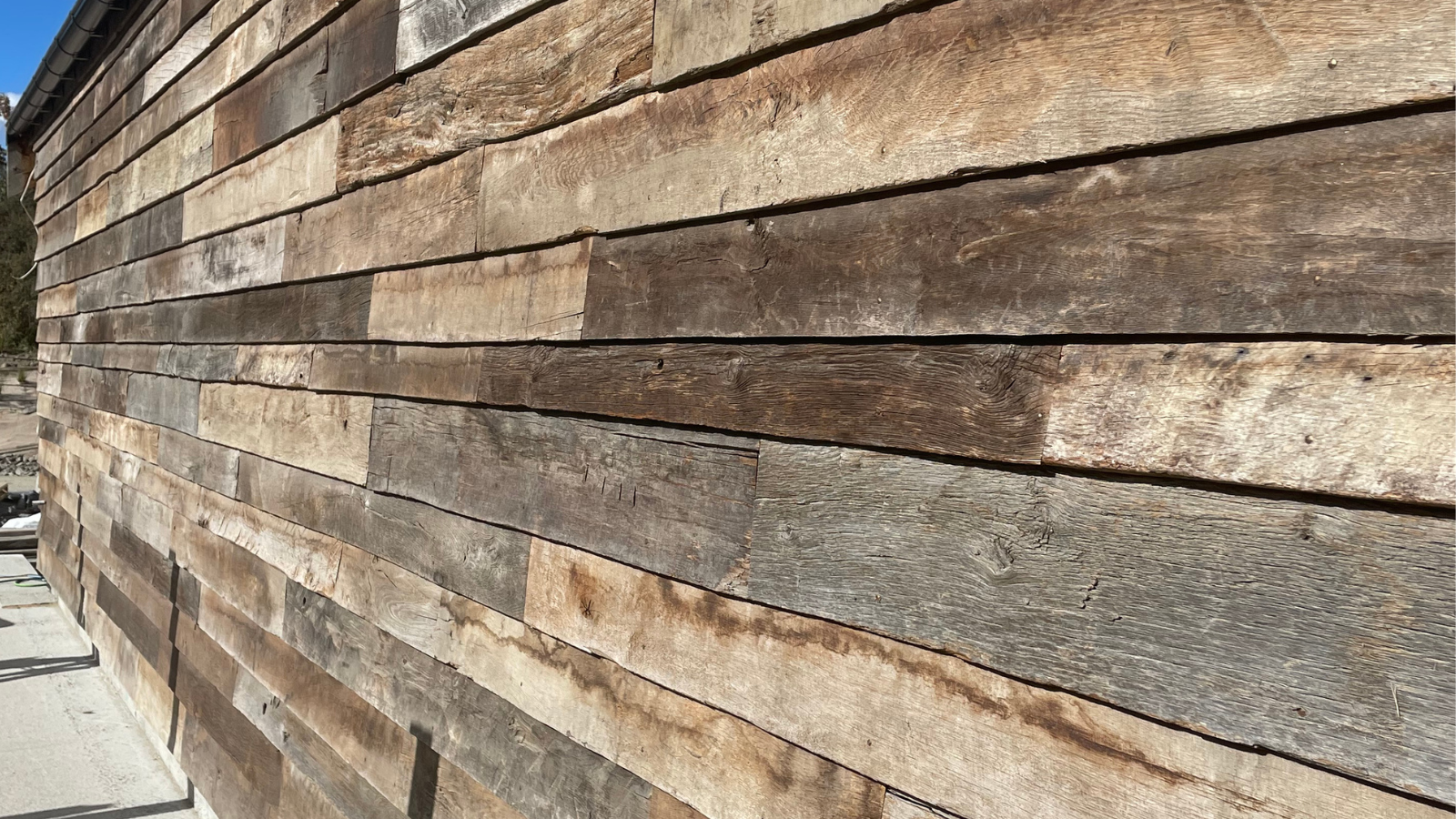 Close view of reclaimed barn wood cladding showing irregular board widths, weathered surfaces and natural grey and brown tonal variation.