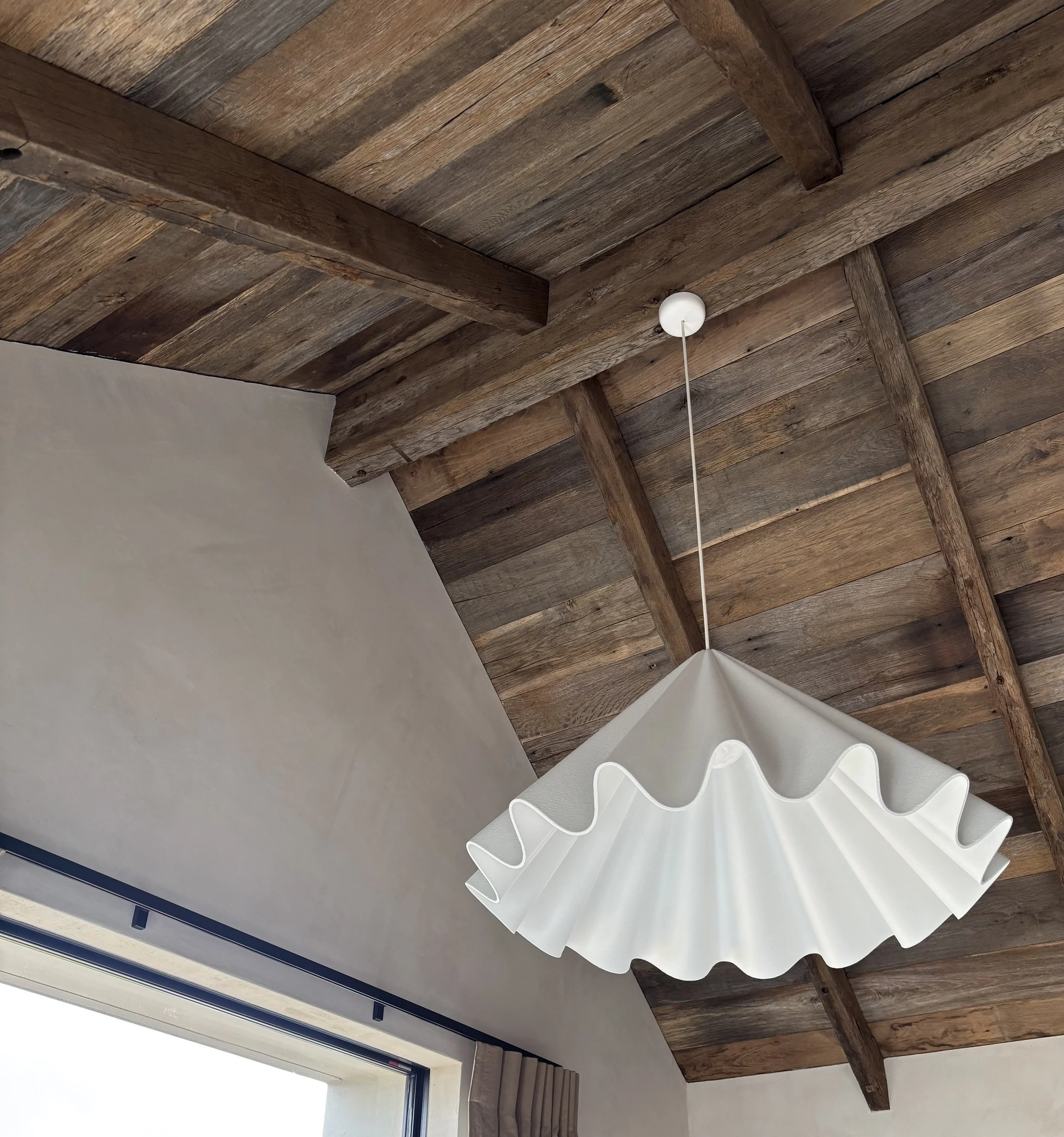 Wooden ceiling with exposed beams, a white pendant lamp hanging from the ceiling, and a window with sheer curtains.