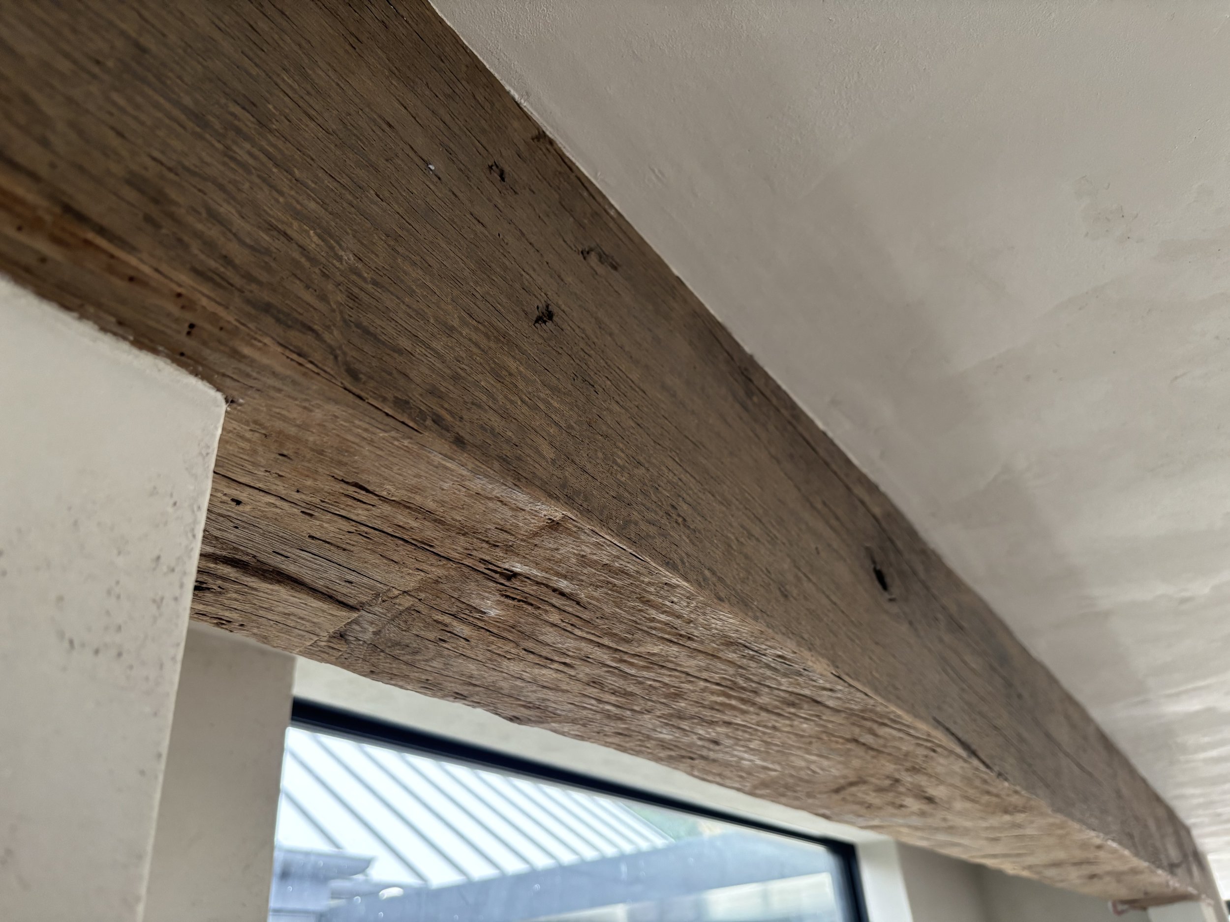 Installed reclaimed oak box beam showing aged grain, natural cracks and rustic surface character. Used to create the appearance of a solid antique oak beam with a lighter, more adaptable form.