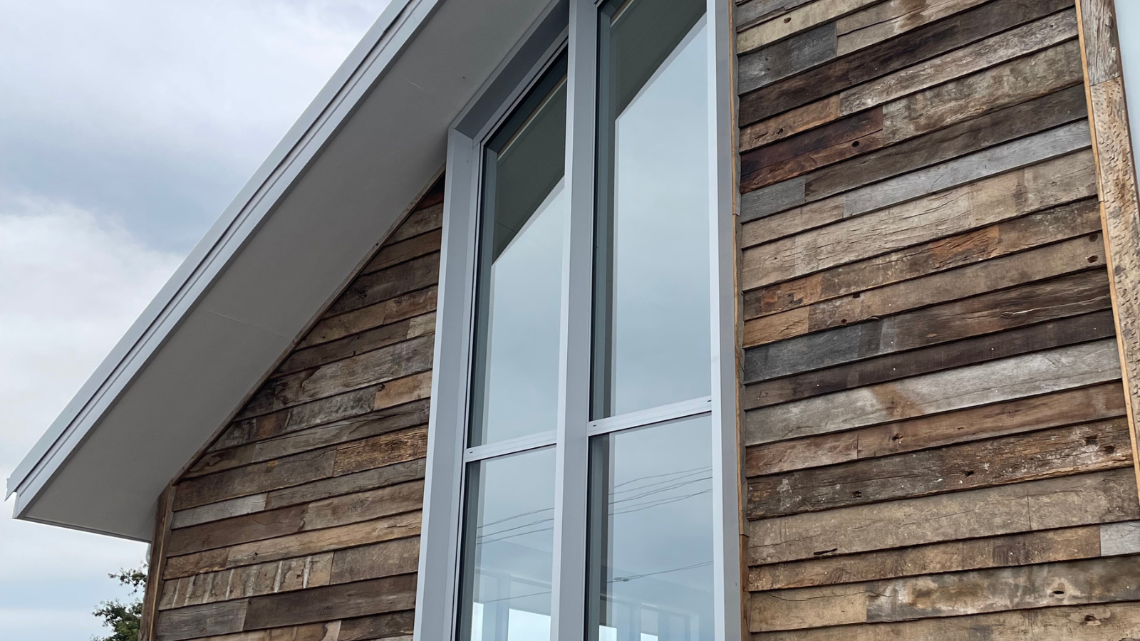 Reclaimed barn wood cladding installed around tall windows on a contemporary residential exterior.