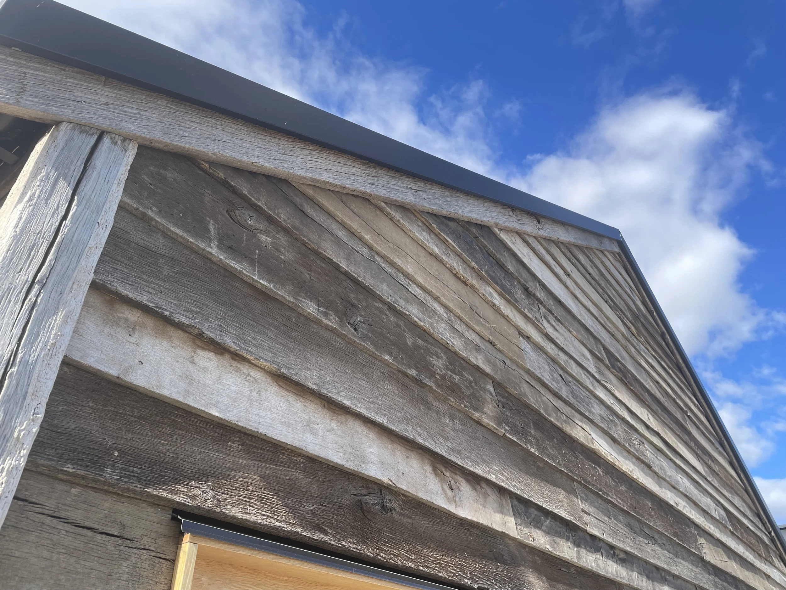 Close-up view of the side of a weathered wooden structure with a metal trim and a blue sky with clouds in the background.
