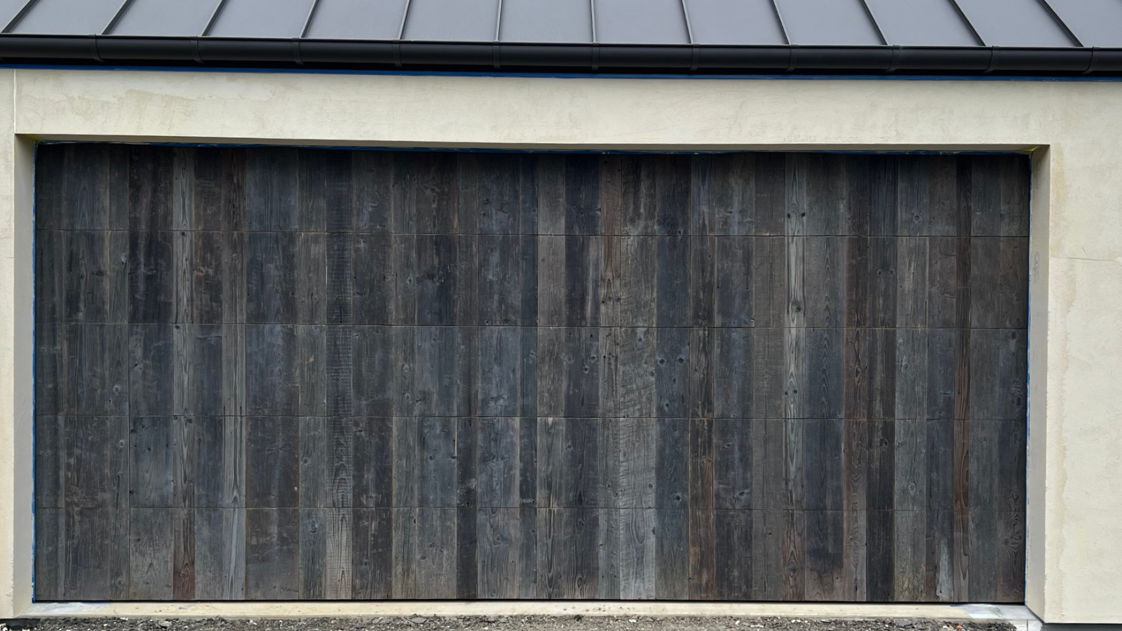 Garage door faced with reclaimed barn wood boards, showing dark weathered tones and natural timber variation.