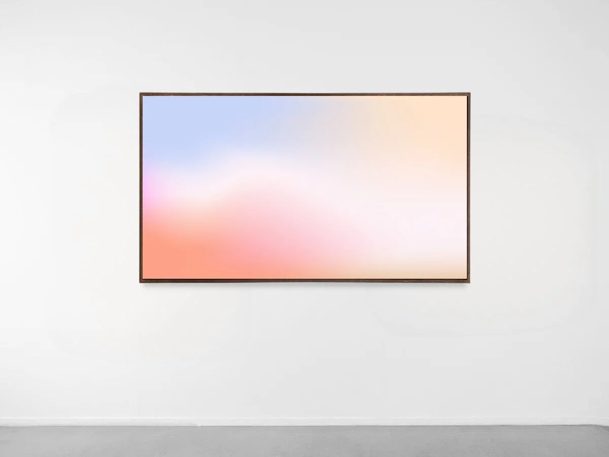 A blank digital screen displaying a blurred gradient of pastel colors, mounted on a white gallery wall.
