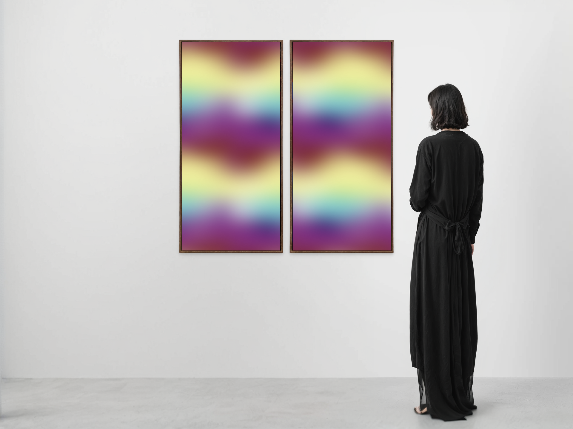 A woman in a long black dress viewing two framed abstract colorful artworks on a white gallery wall.