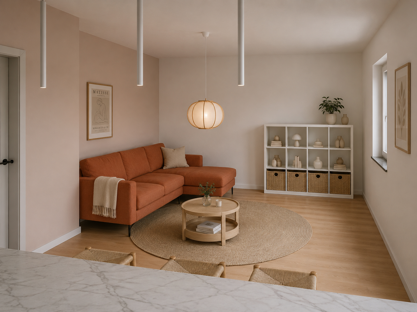Ein Wohnzimmer mit einem orangefarbenen Sofa, einem runden Kaffeetisch und einem weißen Regal mit Körben. Es gibt Wandkunst, eine Pflanze auf dem Regal und eine Deckenleuchte in Form eines papiernen Laternen. Der Raum ist hell und modern gestaltet, mit Holzboden und minimalistischem Dekor.