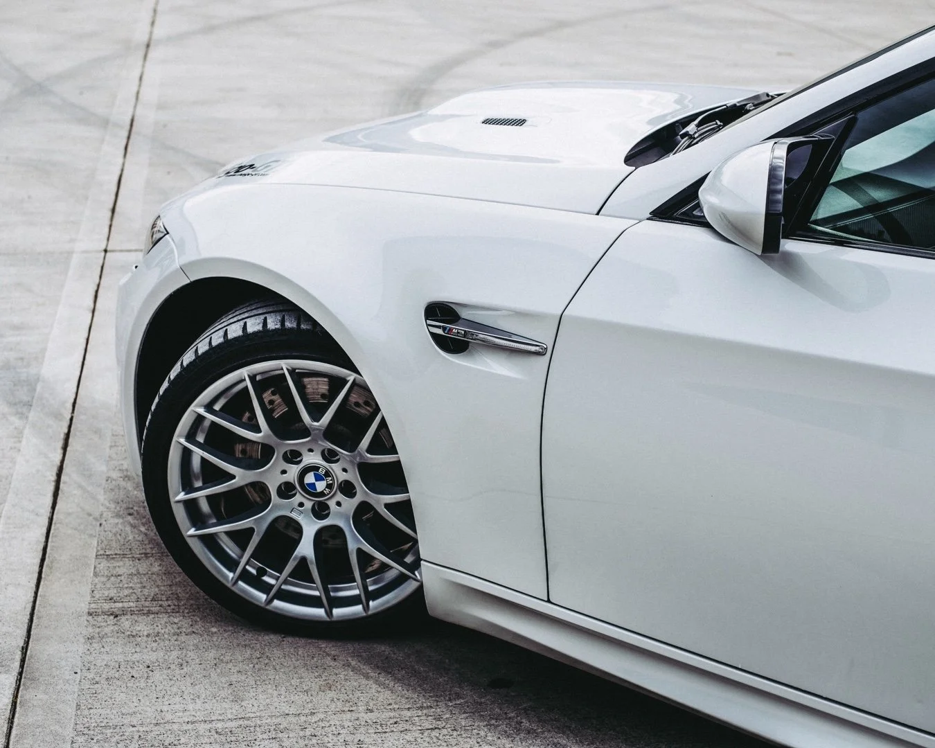 Close-up of a white BMW sports car parked on a concrete surface, showing front part including the wheel, side mirror, and part of the hood.
