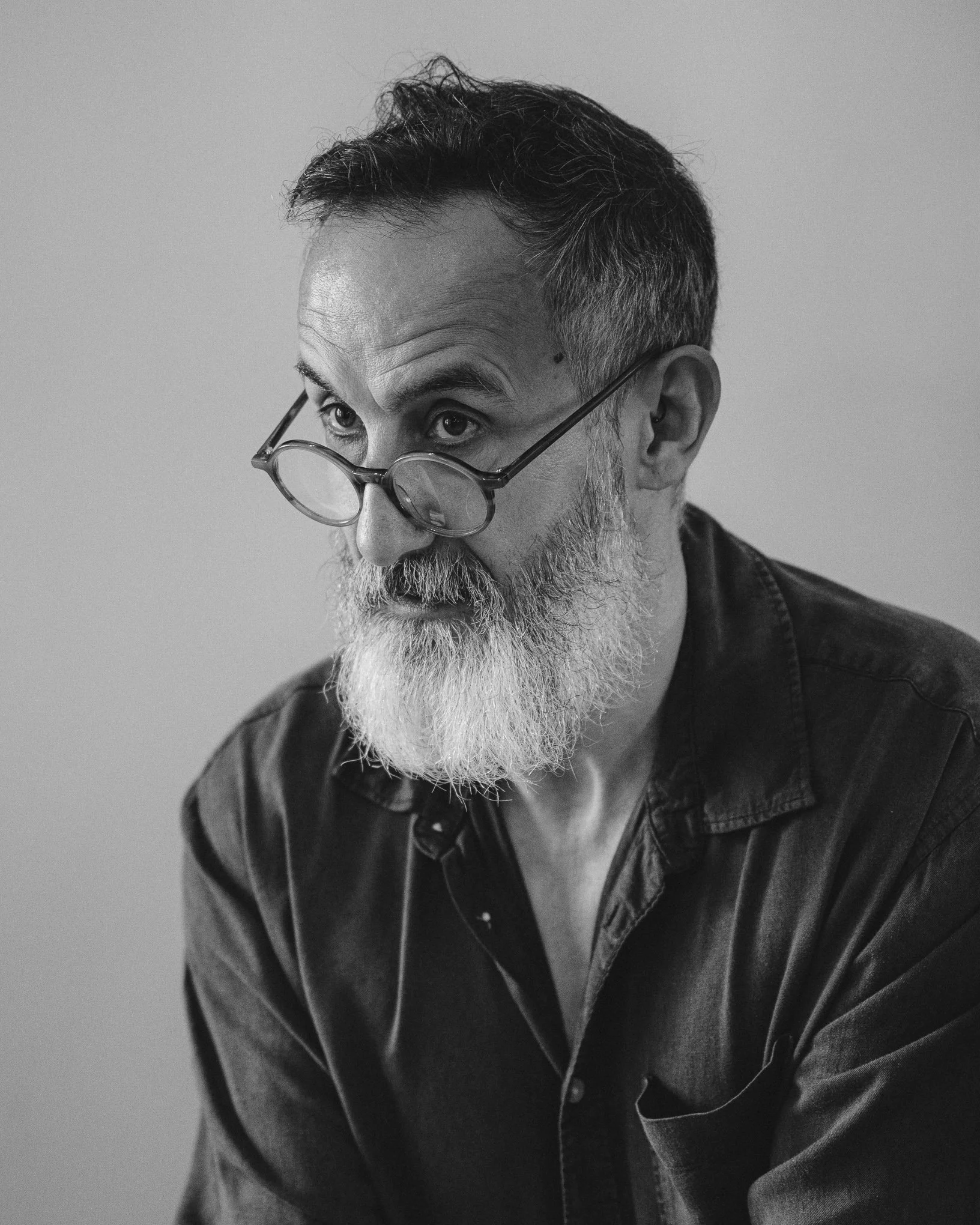 A black-and-white photo of a middle-aged man with glasses, short beard, and mustache, with graying hair, looking slightly to the side against a plain background.