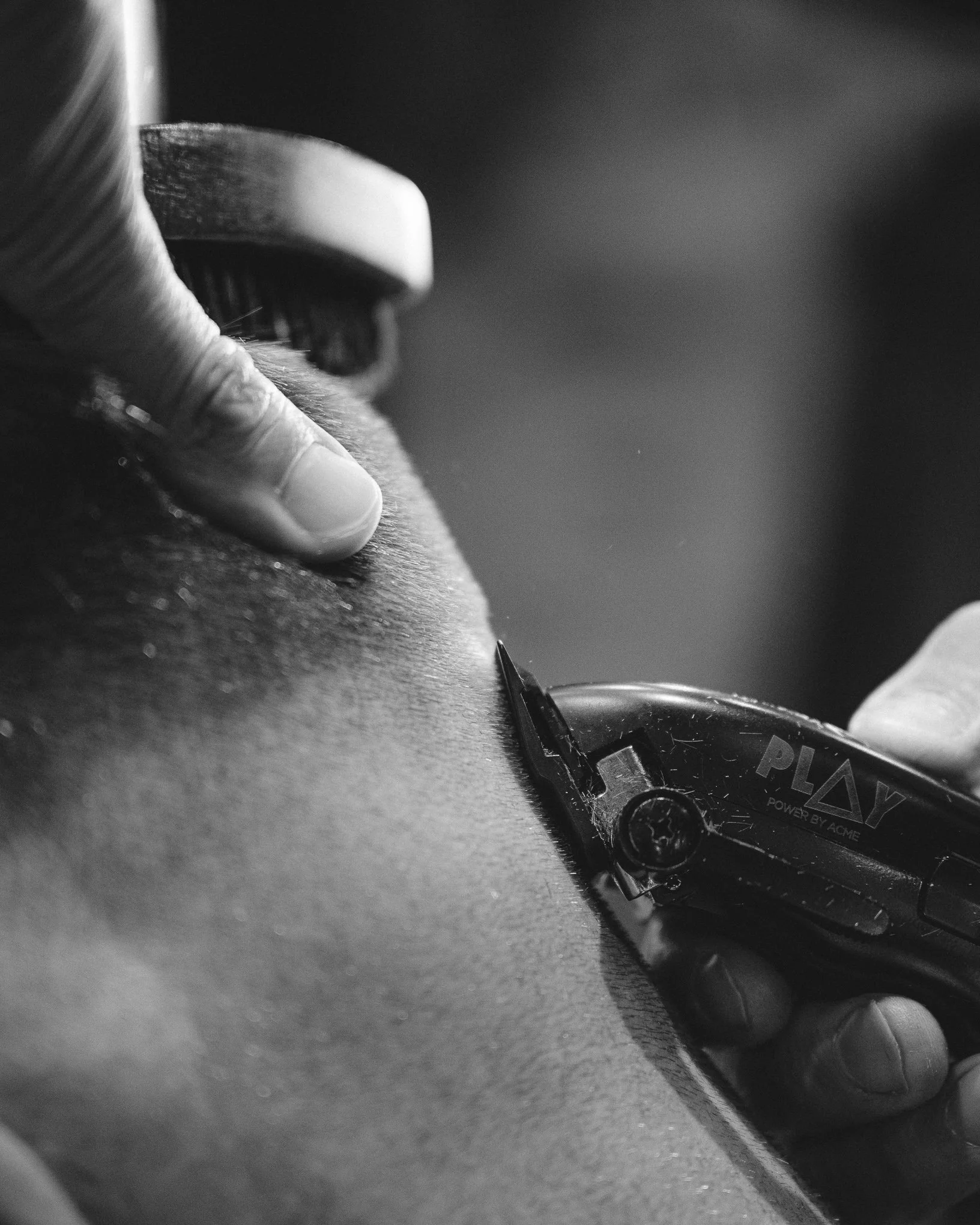 A close-up black and white photo of a person receiving a tattoo on their skin, with a tattoo machine and a needle visible.