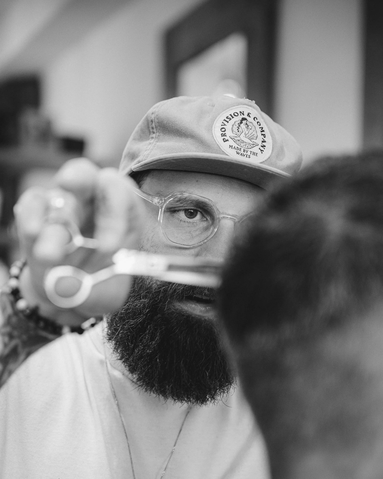 A person with glasses, a beard, and wearing a cap with the logo 'Provision & Company, Made by the Waves' taking a selfie, with the focus on their face and cap.