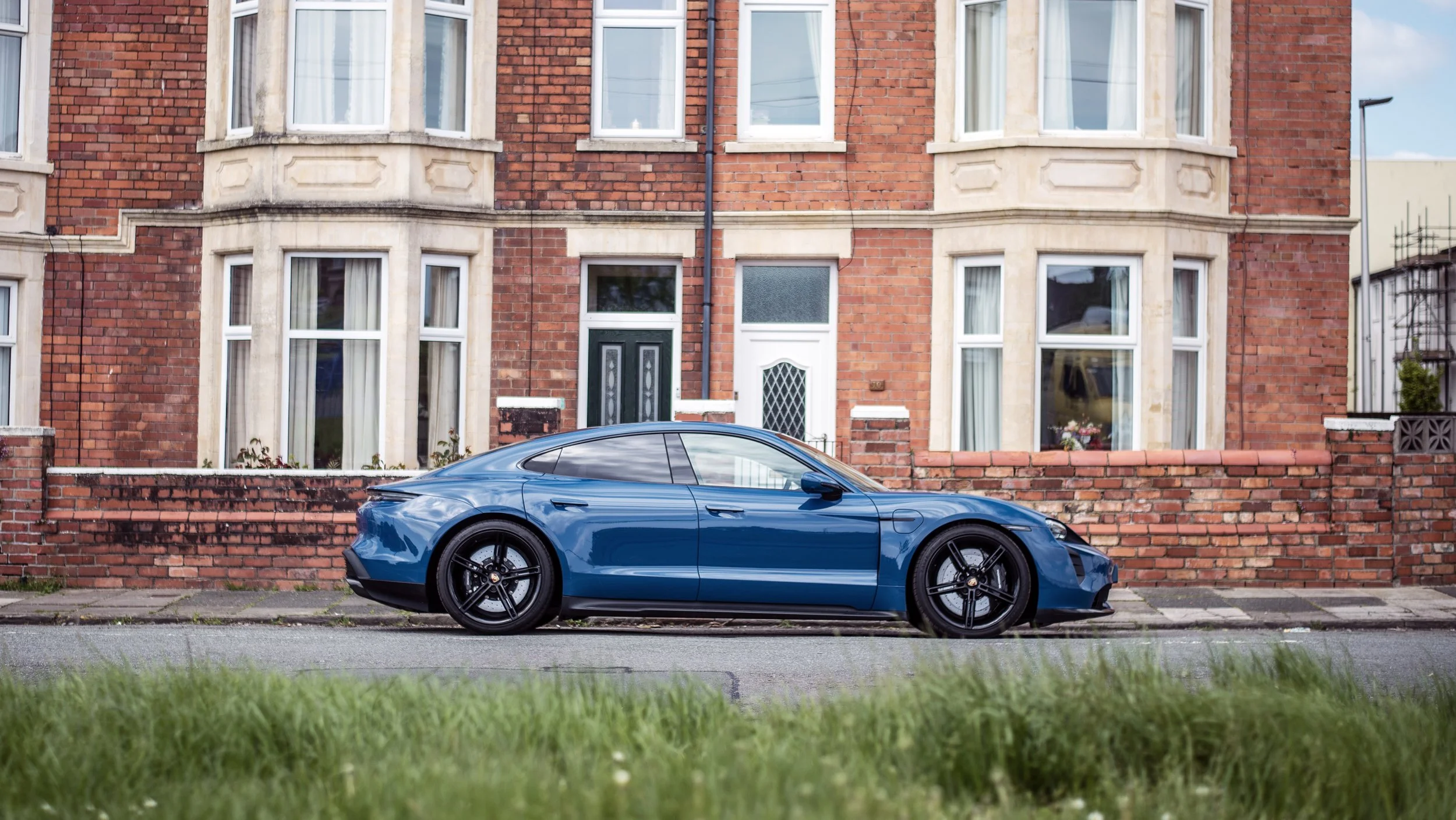 A blue sports car parked on the street in front of a red brick residential building with bay windows.