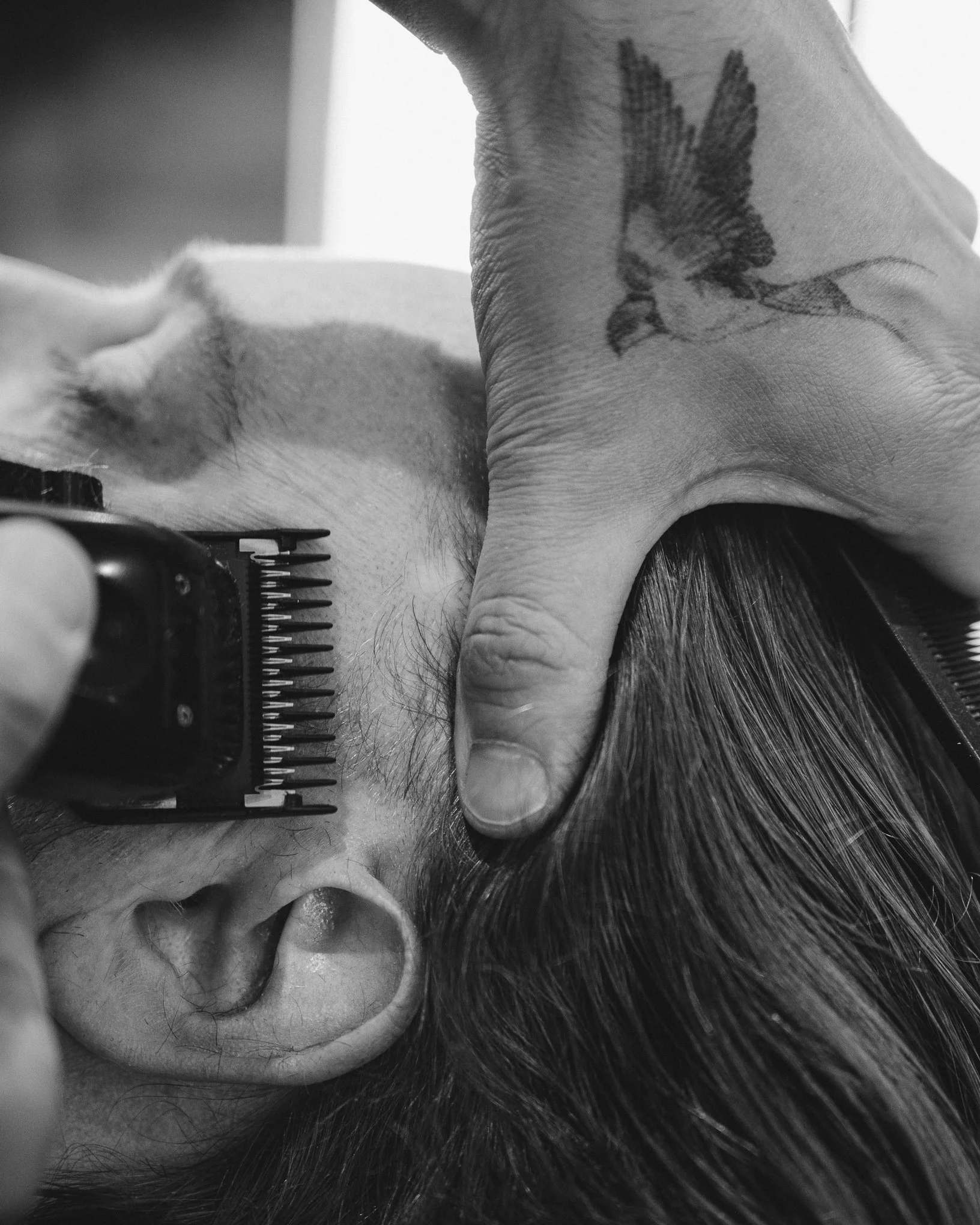 A person receiving a haircut, with scissors and comb visible, and a tattoo of leaves on their hand.