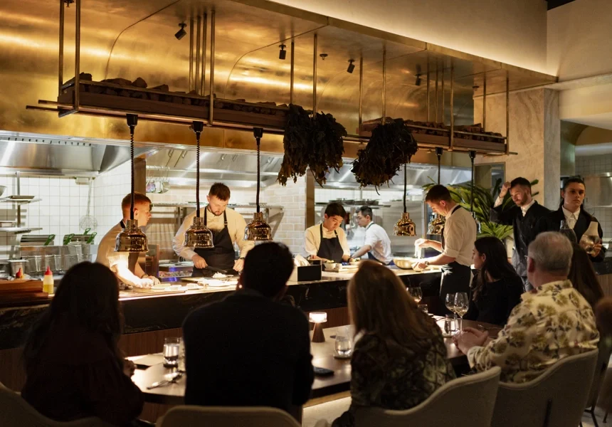 People dining at a restaurant with open kitchen and chefs preparing food behind the counter.