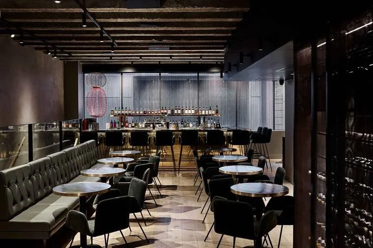Empty modern bar and seating area with tables, chairs, and bar counter in a dimly lit restaurant.