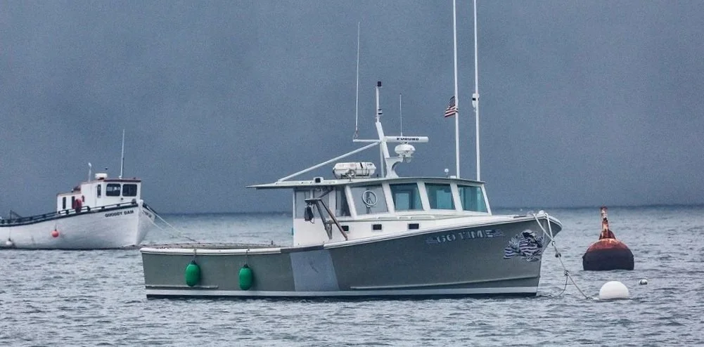 A gray motorboat named '440 TIME' anchored near a buoy on a body of water, with a larger white boat named 'GROOVY DAY' in the background, and an overcast sky.