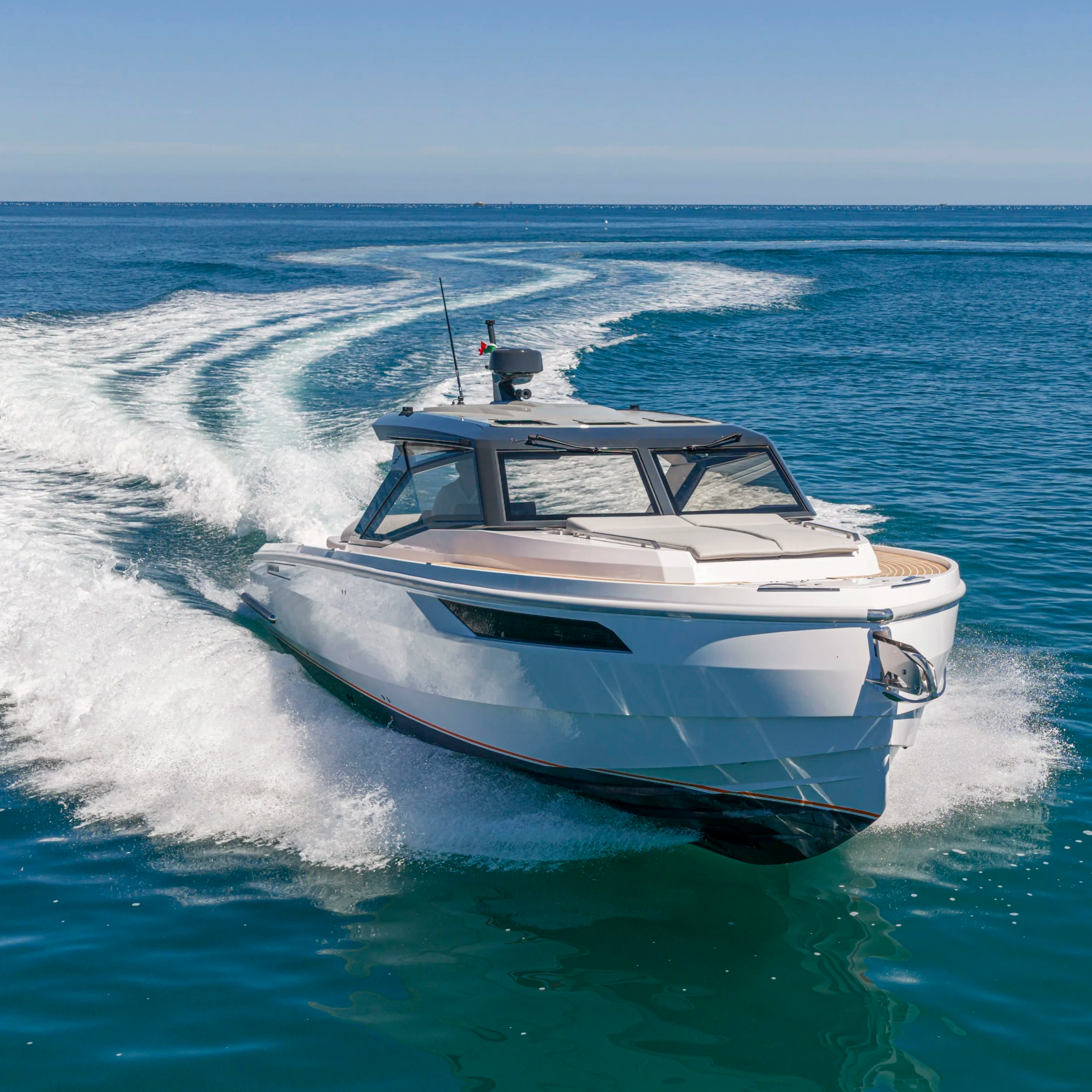 A boat speeding on the ocean, leaving a trail of white foam behind, with a clear blue sky and calm sea in the background.
