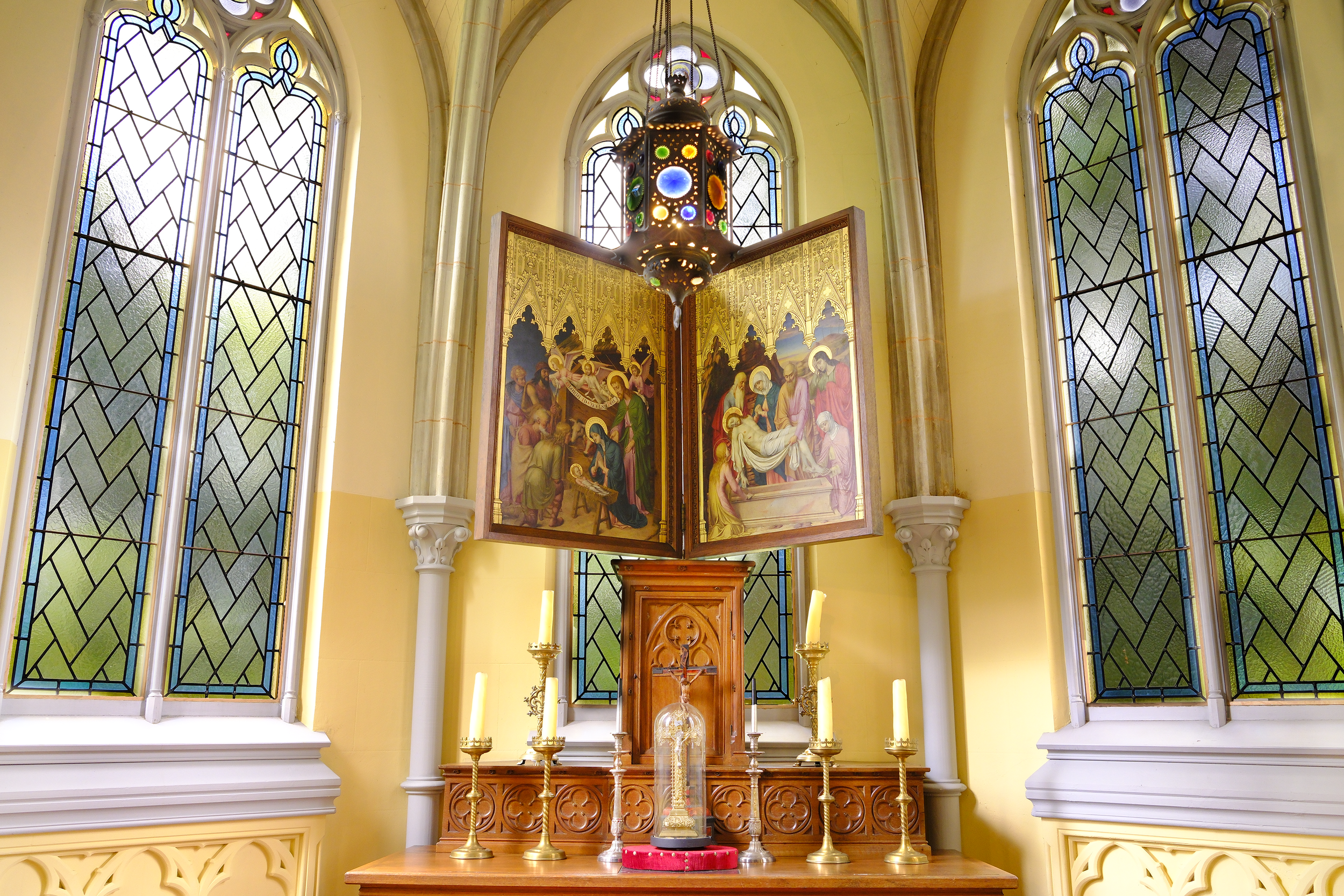 Interieur van een kerk met grote gekleurde glas-in-loodramen, een altaar met een schilderij en een hanglamp.  | Kasteeldomein Battenbroek | Evenementenlocatie in Mechelen