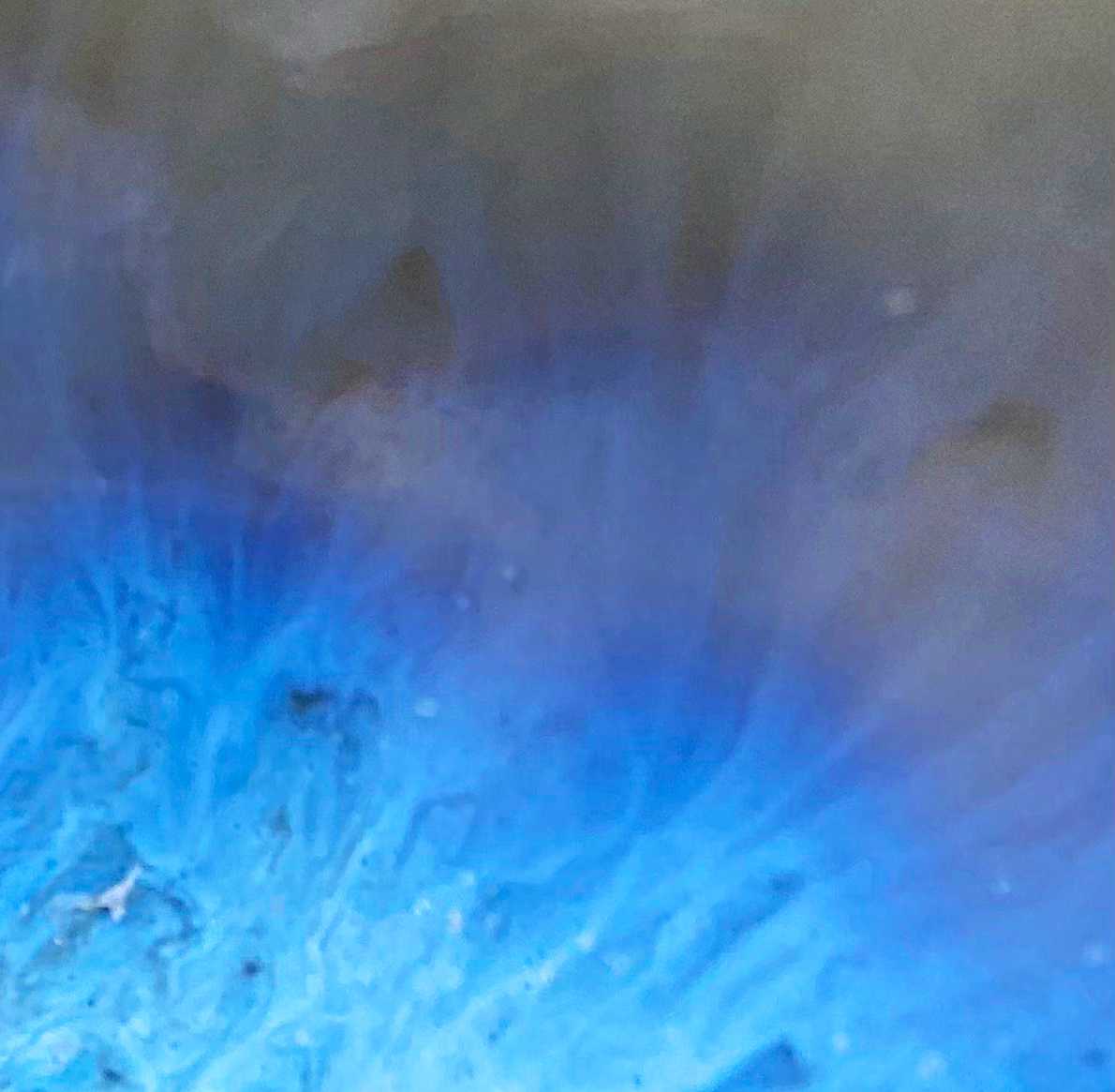 Close-up of a surface with a gradient from blue to dark gray, showing some texture and small irregularities.