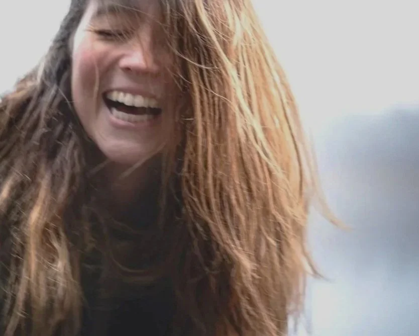 Close-up of a woman with long, wavy red hair smiling and laughing.