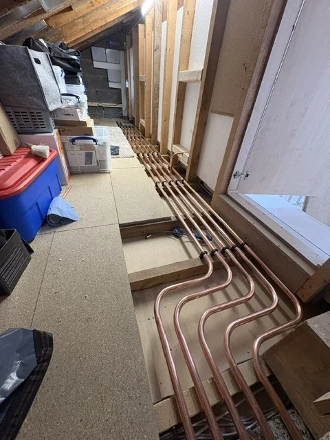 Copper plumbing pipes installed along the floor under construction in an unfinished space with exposed insulation and wall framing.
