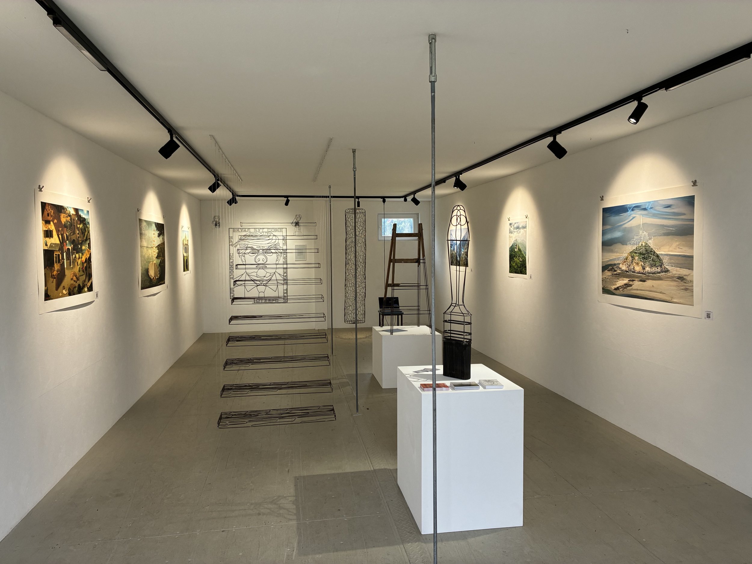 Ausstellungsraum mit Fotografien an weißen Wänden, Skulpturen auf Podesten, und einem Gitterrahmen in der Mitte des Raumes.