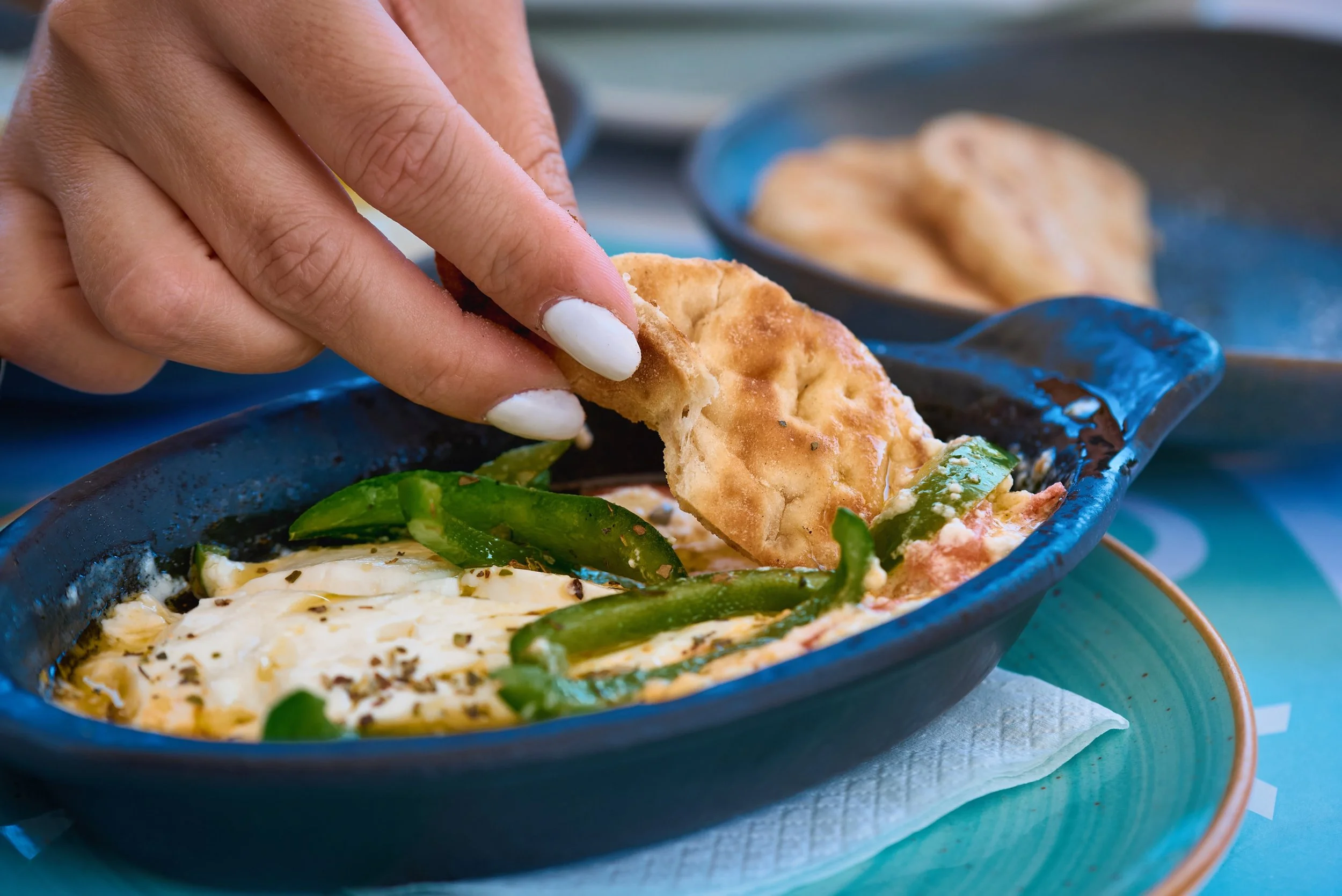 Close-up of a hand with white nail polish picking up a taco shell from a black dish filled with eggs and green chili peppers.