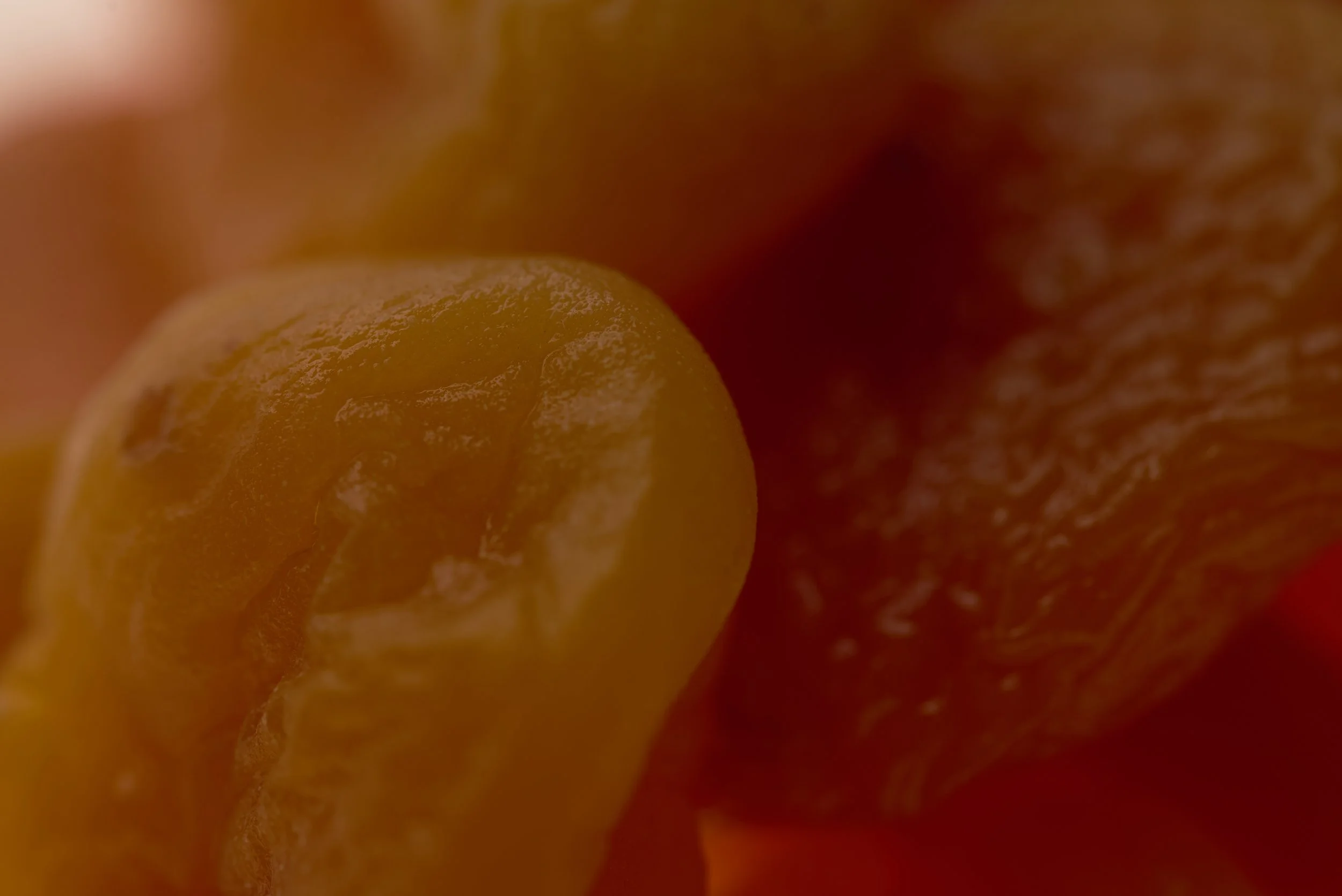 Close-up of yellow and red fruits, possibly citrus, with textured surface and partially visible background.