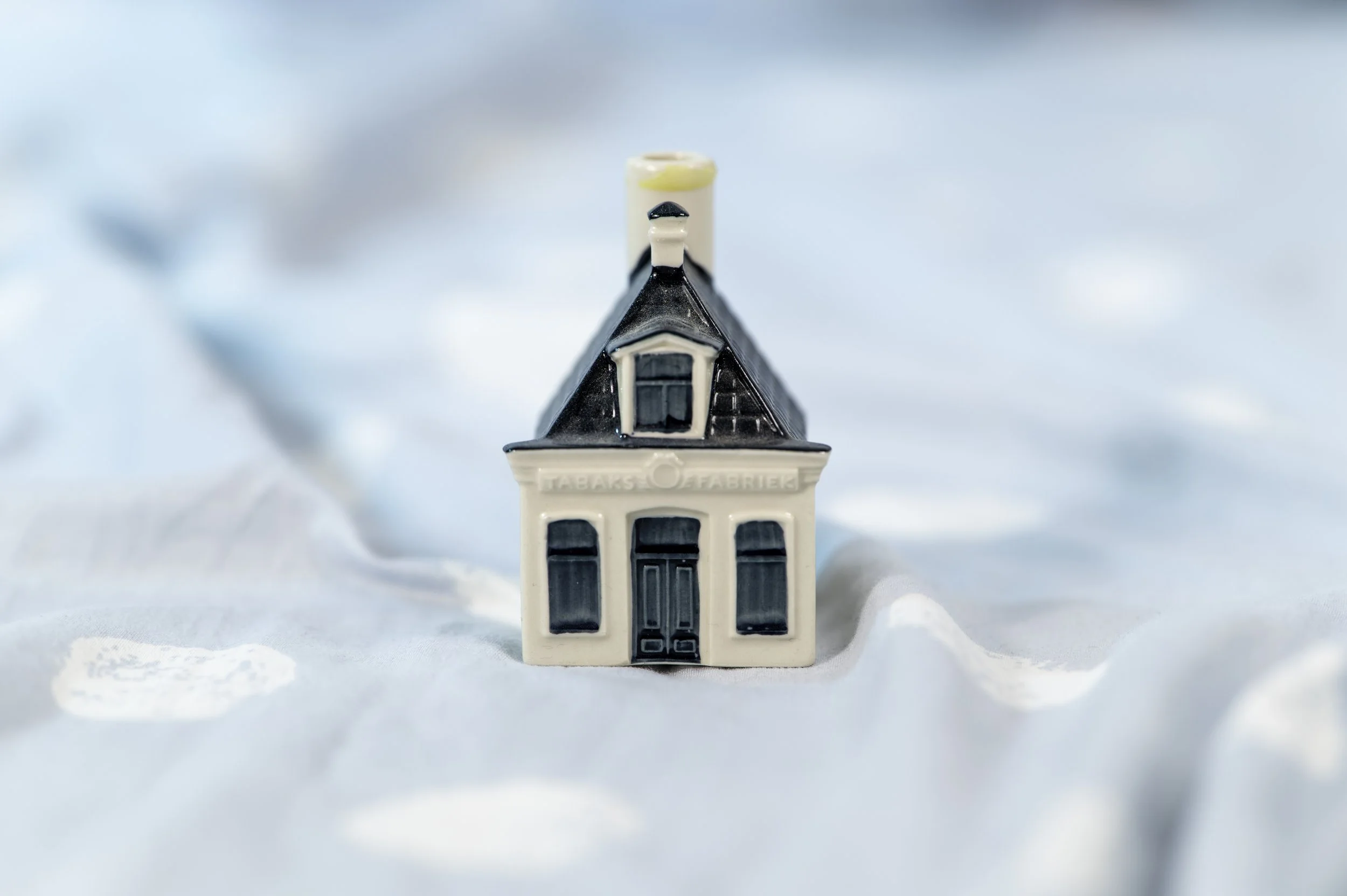 Miniature ceramic house with black roof, white walls, and black window and door details, set against an icy blue background.