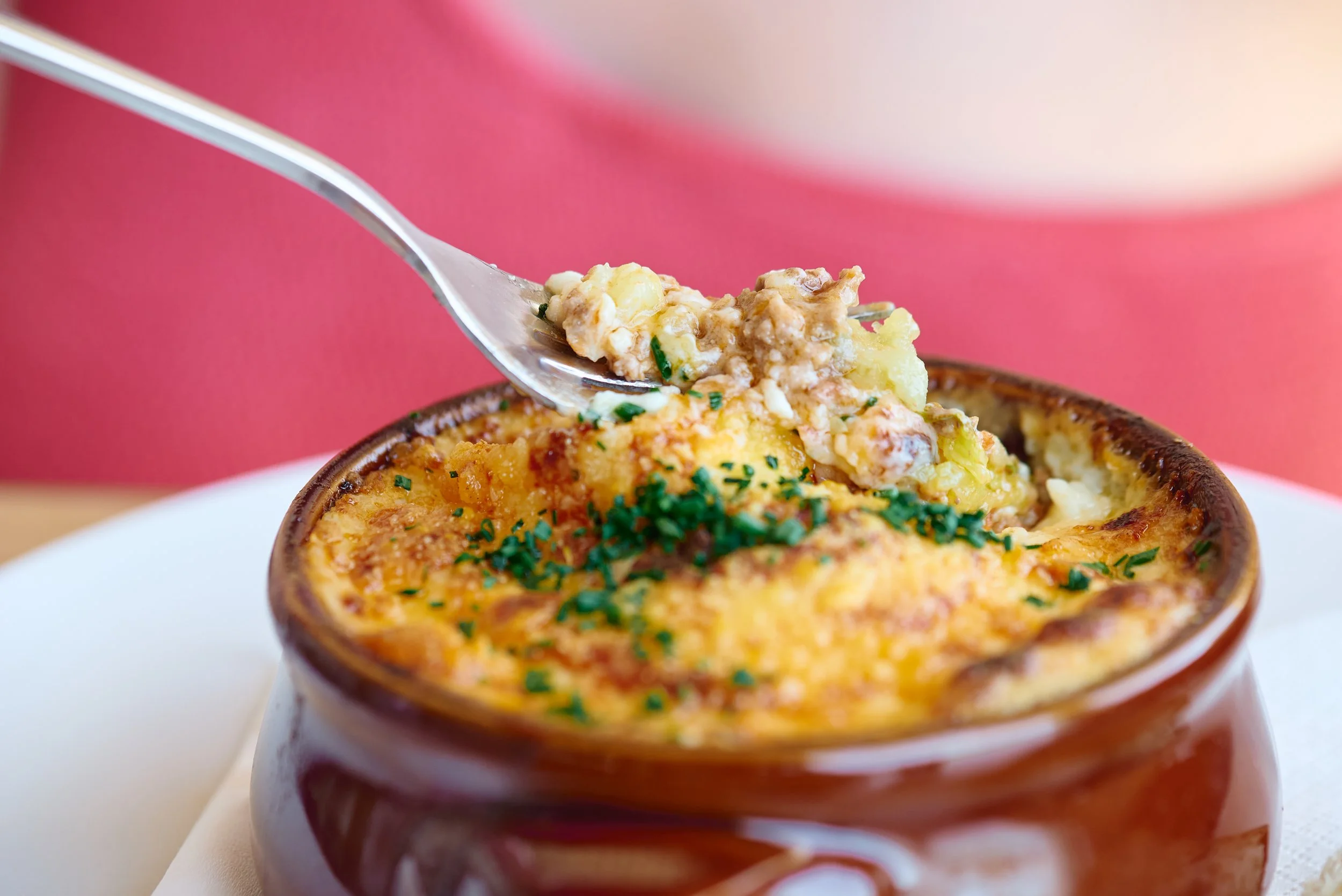 A small brown ramekin filled with baked macaroni and cheese garnished with chopped chives.