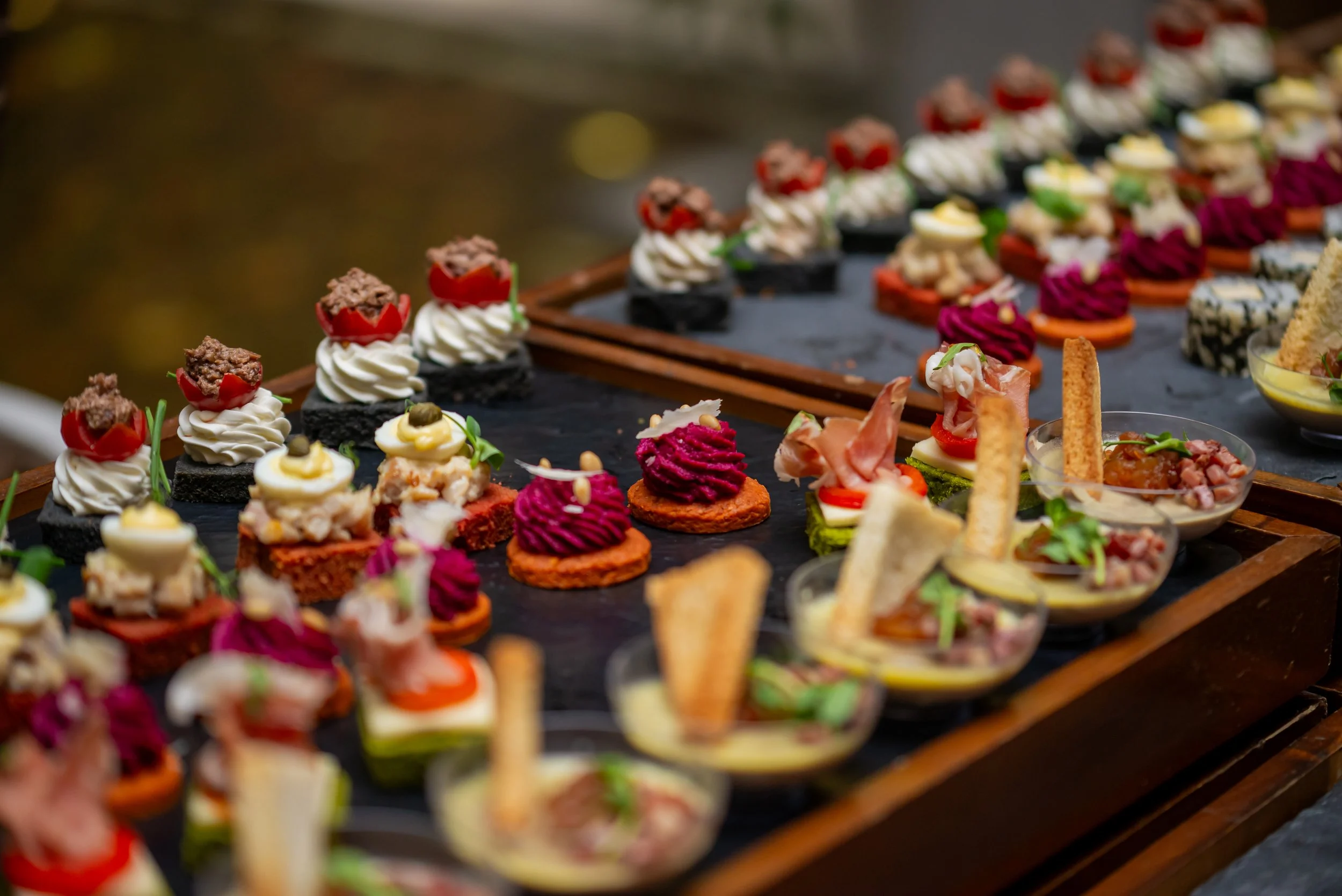 Assorted savory canapés and appetizers on a wooden serving tray.