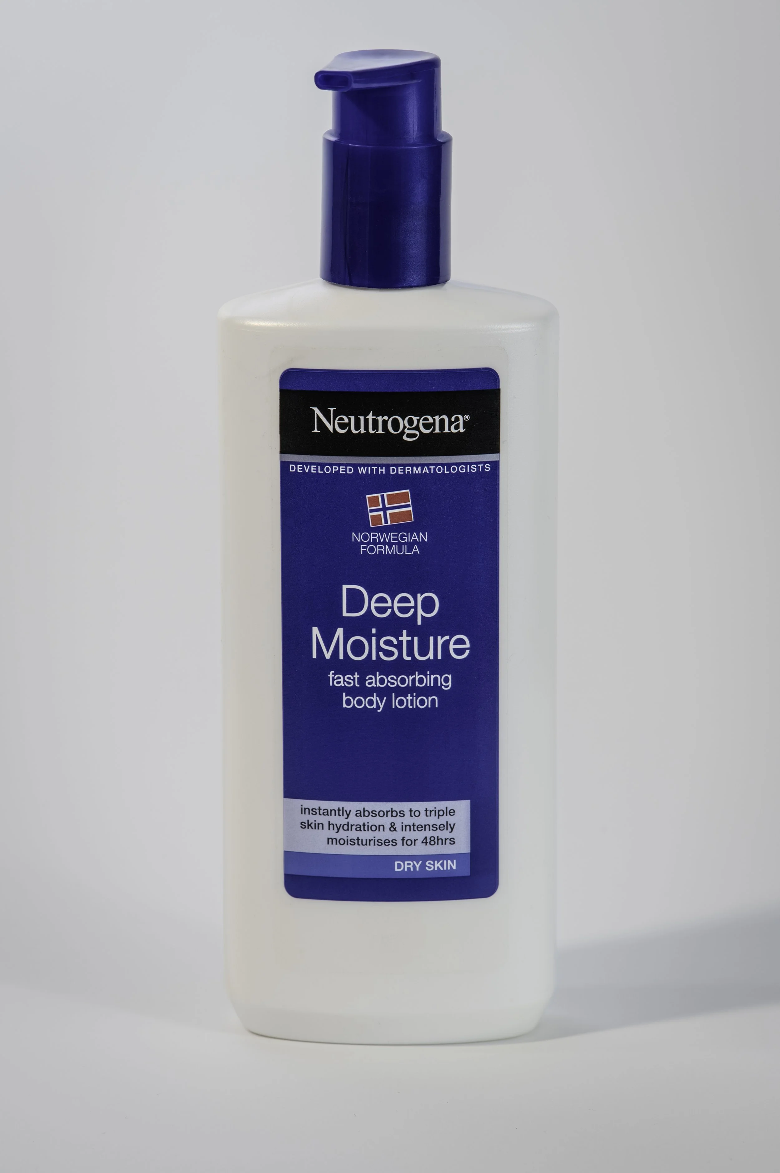 Bottle of Neutrogena Deep Moisture body lotion with a blue cap and a label indicating it is for dry skin, developed with dermatologists, and designed for fast absorption.