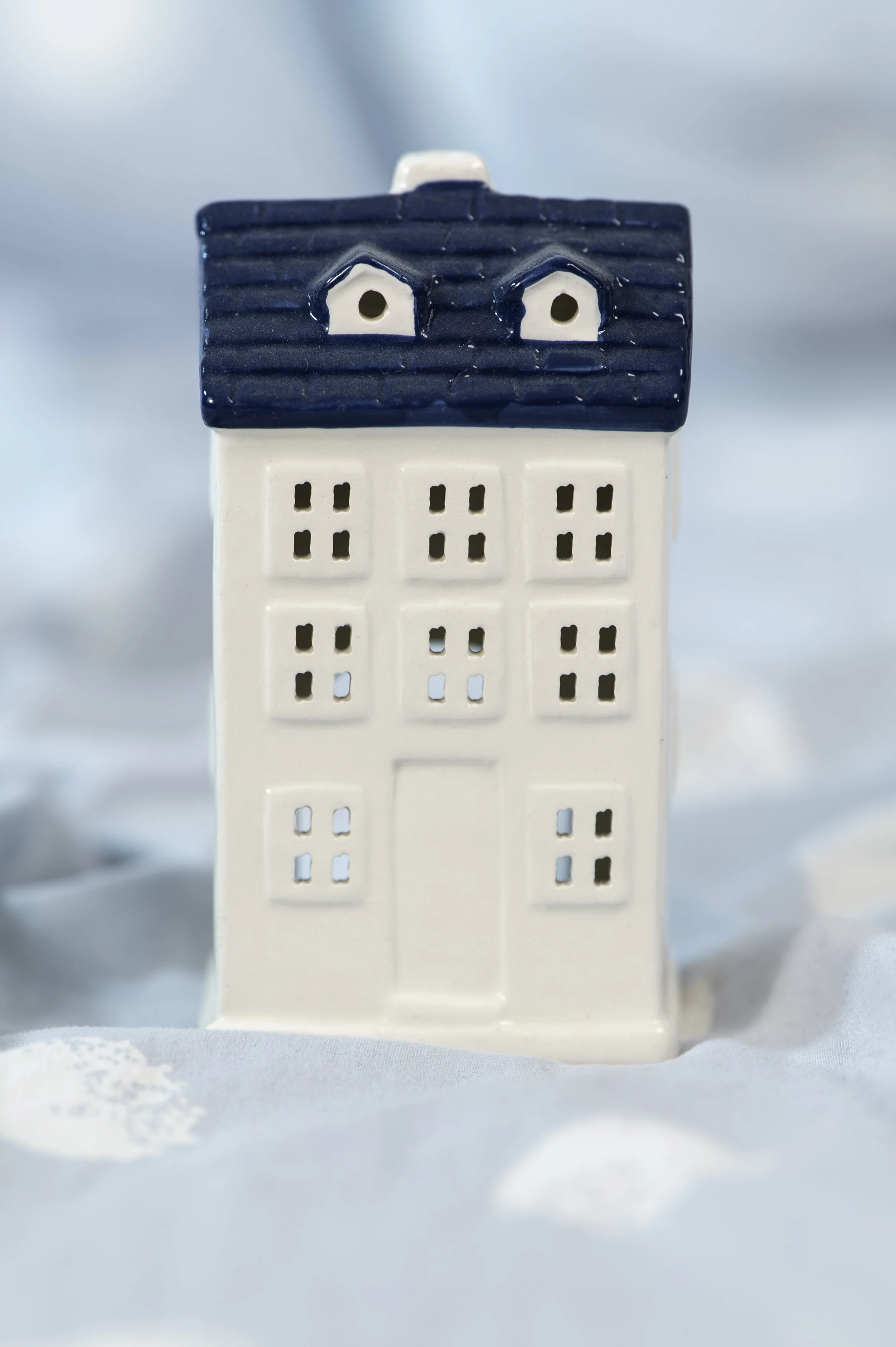 A ceramic miniature house with a dark blue roof, white walls, and small square windows, set against a soft background.