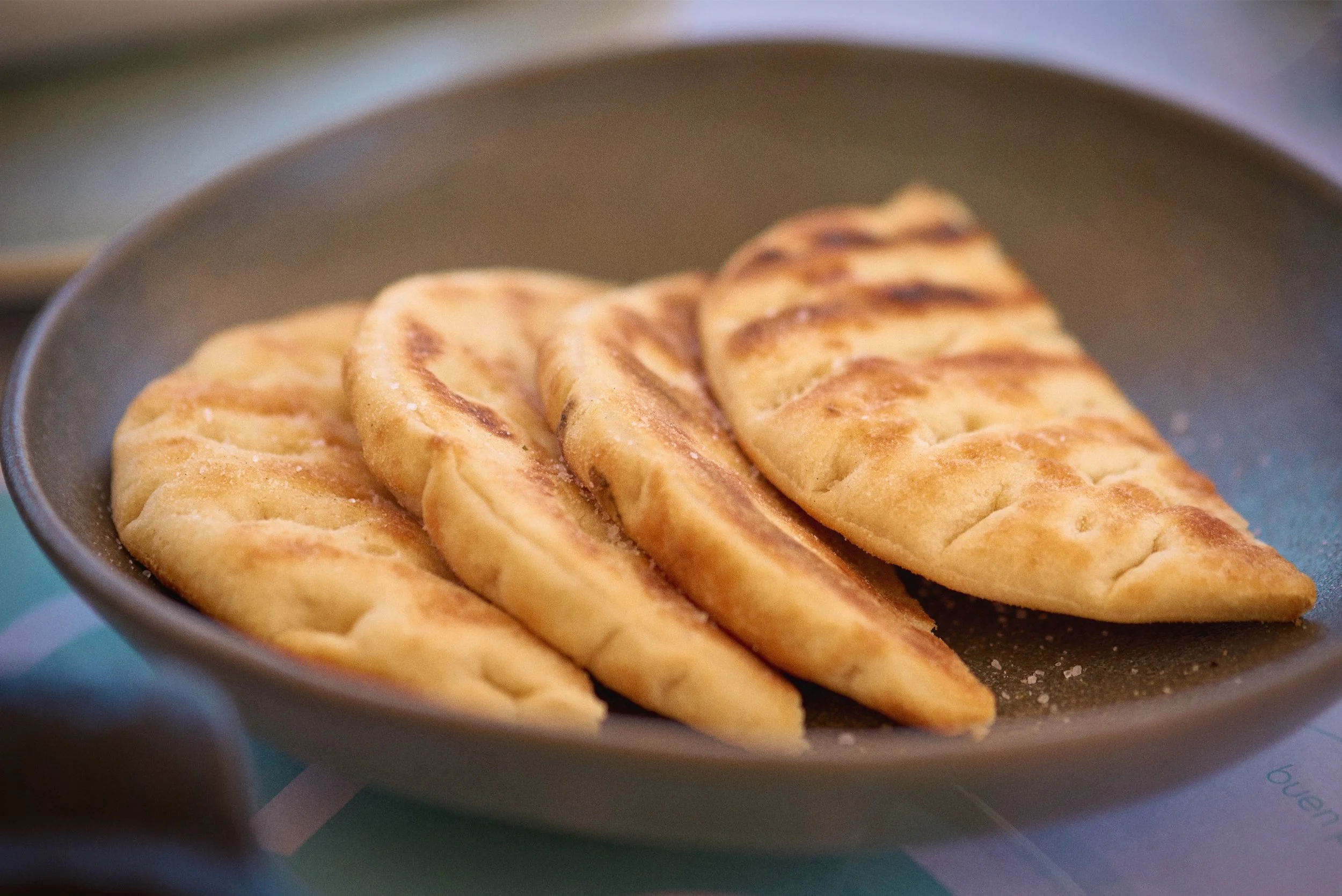 Close-up of grilled flatbread on a dark plate.