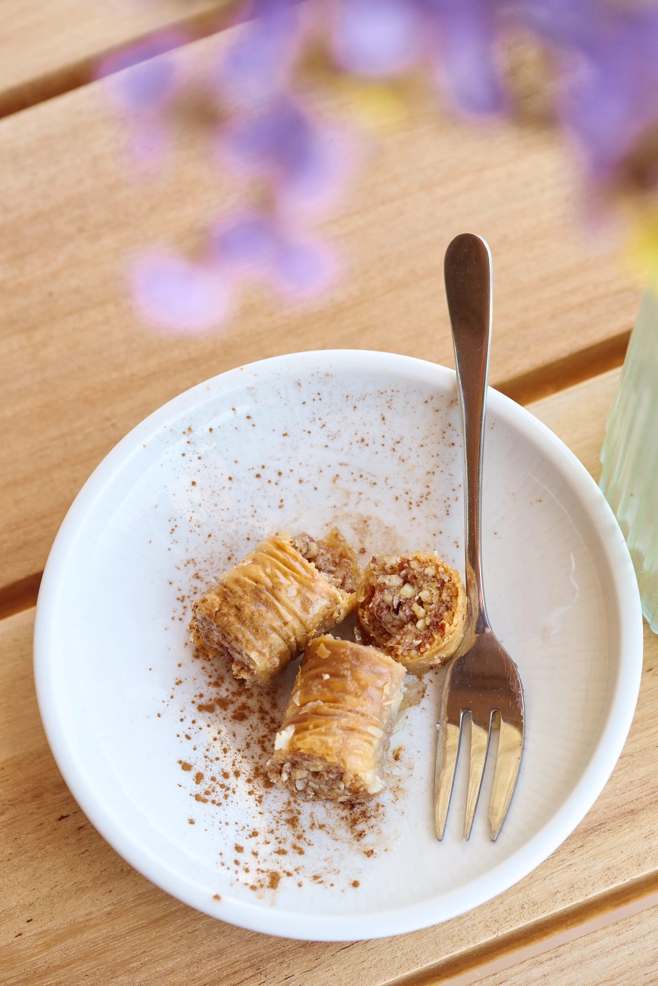 A white bowl with cinnamon sticks rolled up and filled with chopped nuts, sprinkled with cinnamon powder, on a wooden table with a fork.