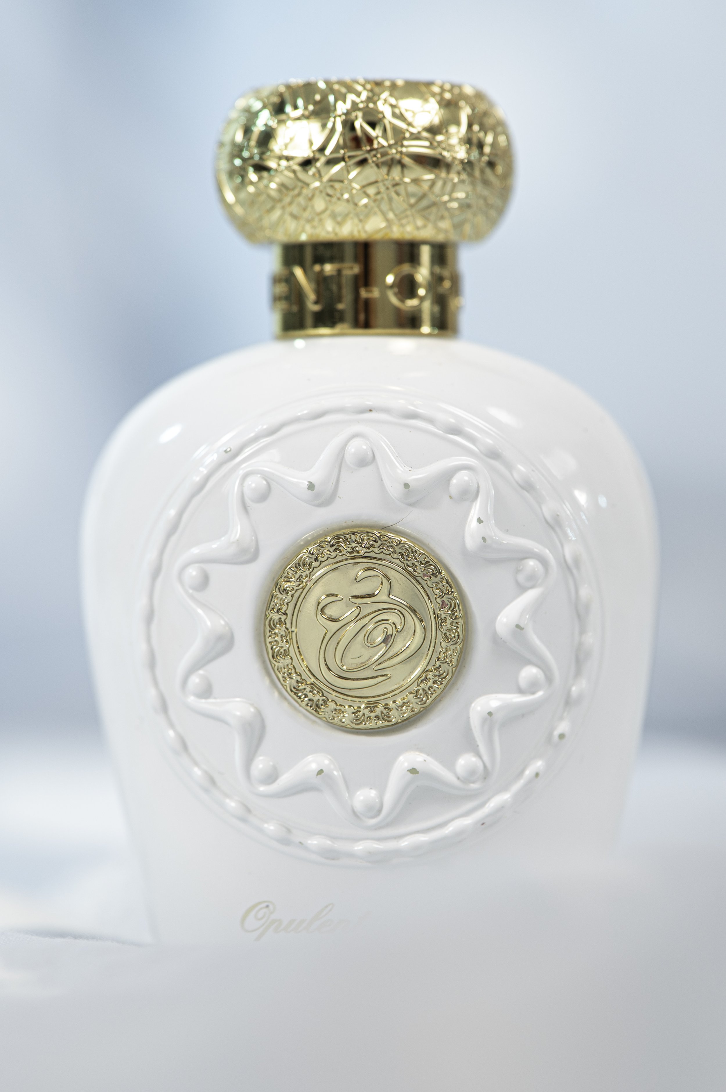 Close-up of a white perfume bottle with gold accents, featuring intricate designs and the word 'Opale' on the front.