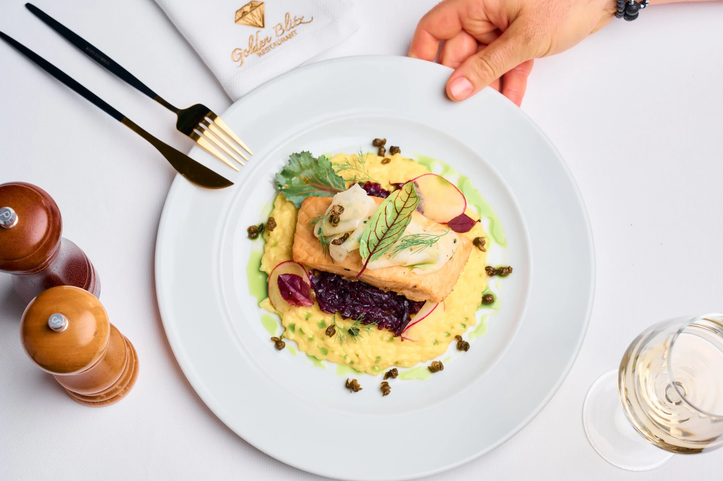 Plate with cooked salmon, mashed potatoes, mixed greens, radishes, and purple cabbage at a restaurant table.