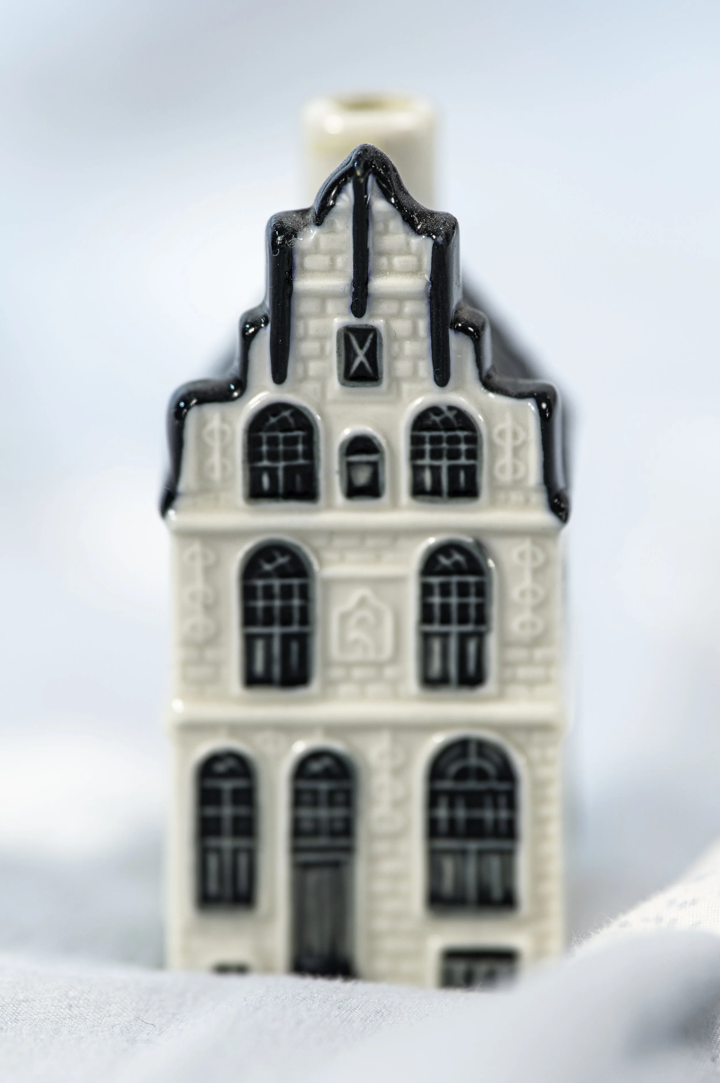 Ceramic house-shaped object with black accents and details of windows and doors, positioned on a white surface with a light blue background.