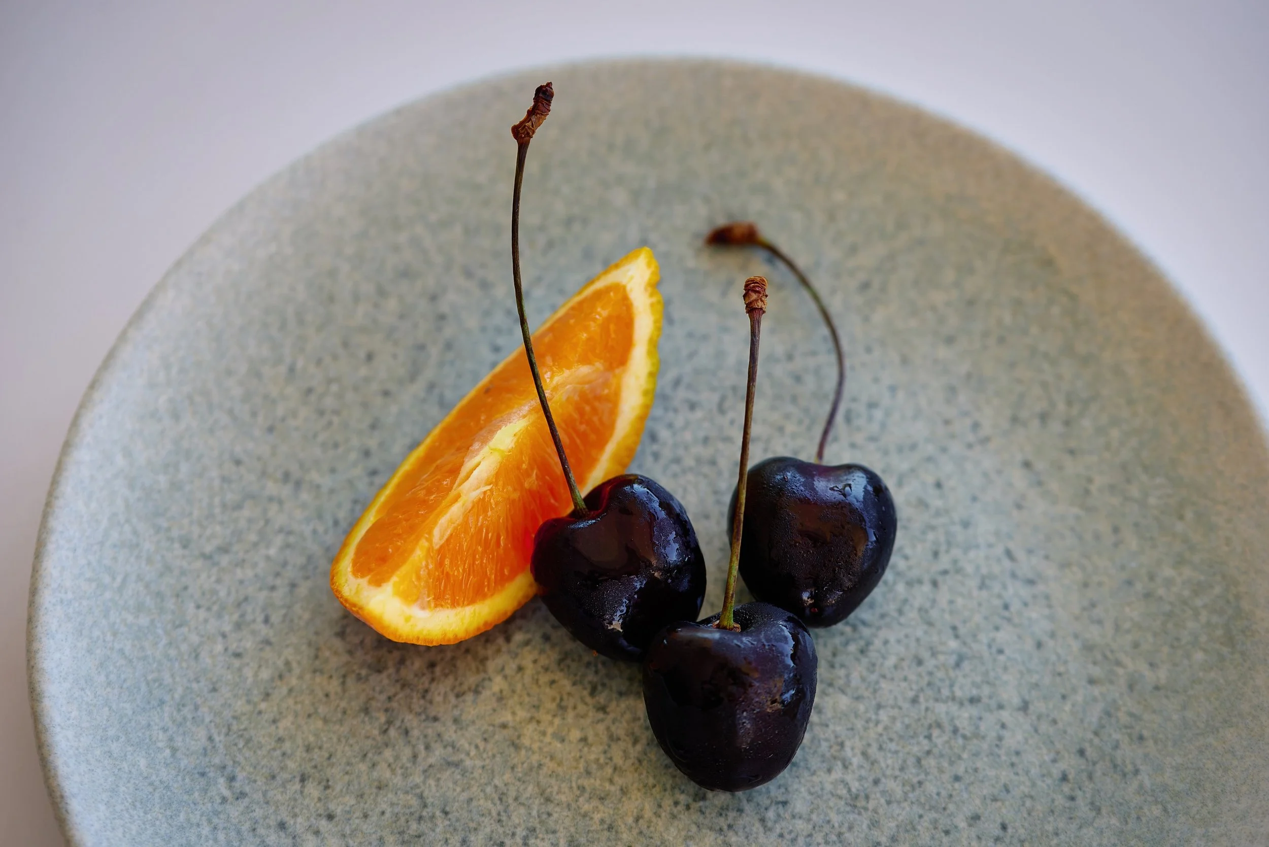 Close-up of a desert plate with three black cherries and a wedge of orange.