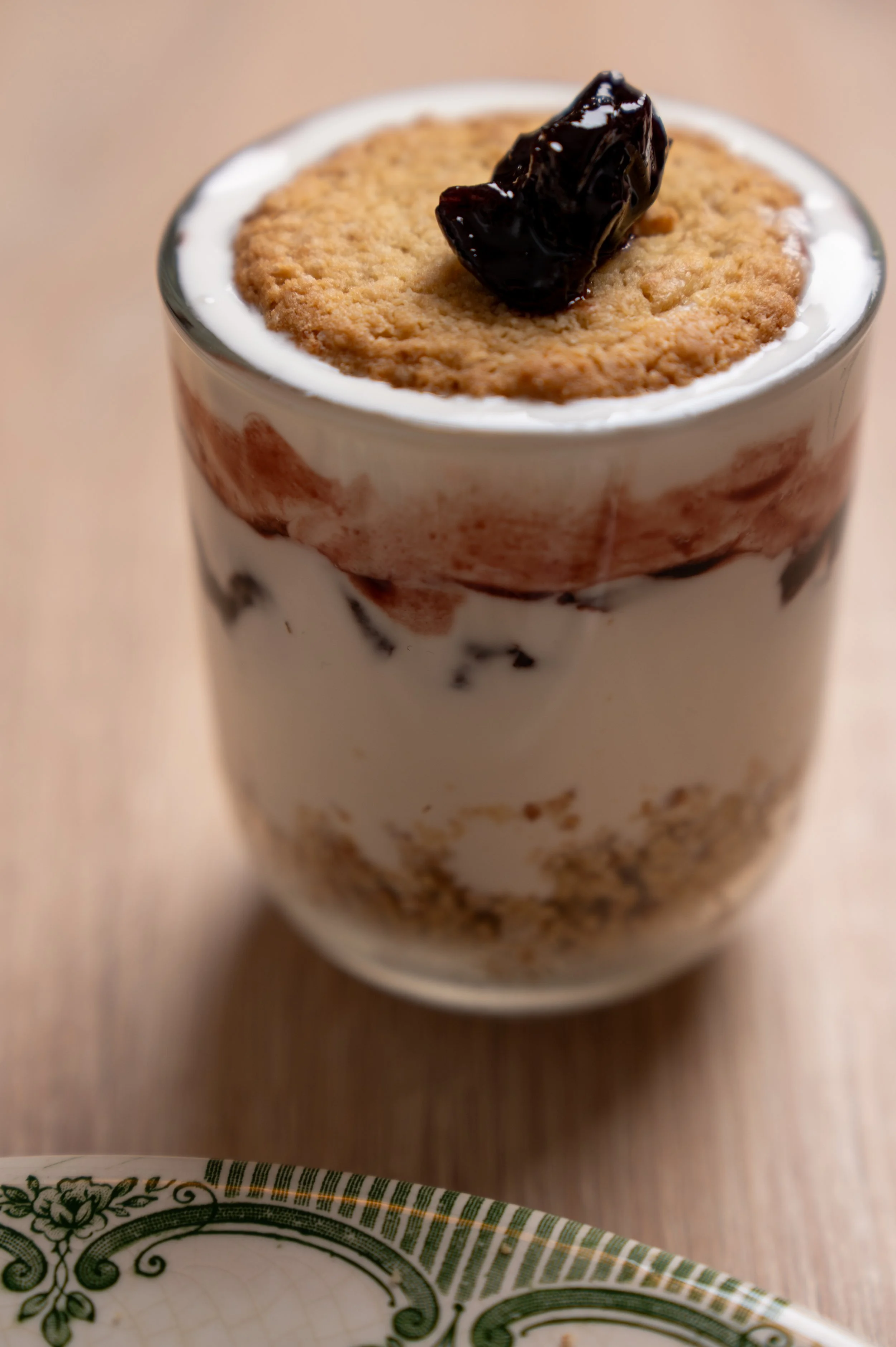 A glass filled with a layered dessert, topped with a cookie and a piece of cherry.