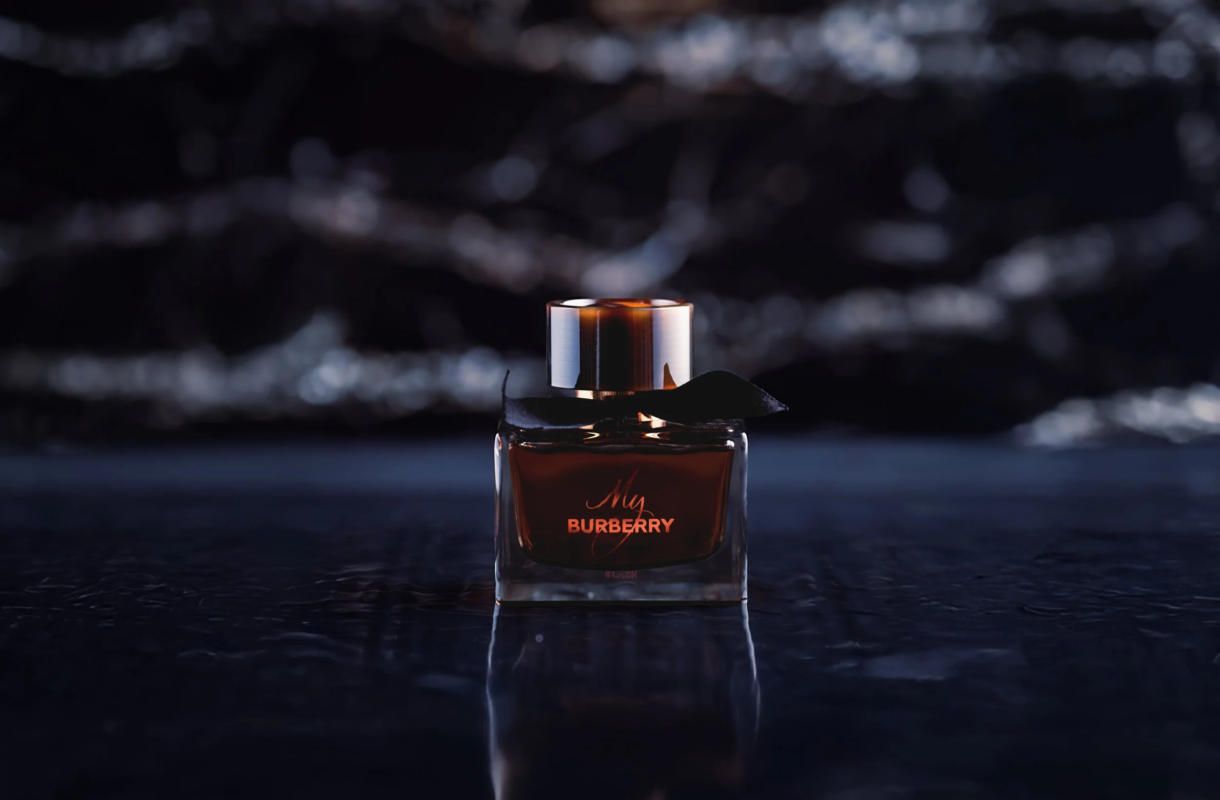 A bottle of Burberry Black perfume placed on a reflective surface with a dark, blurred background.