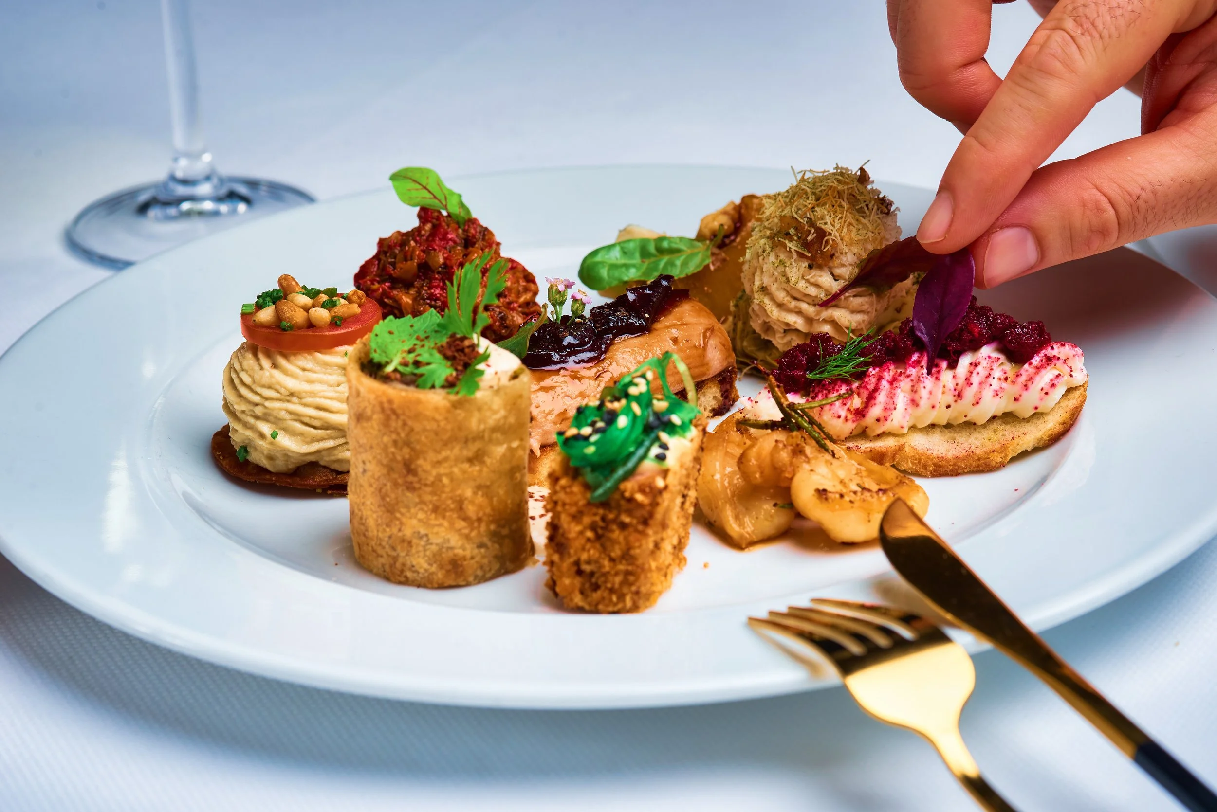 Assorted gourmet appetizers on a white plate, with a glass of white wine in the background.