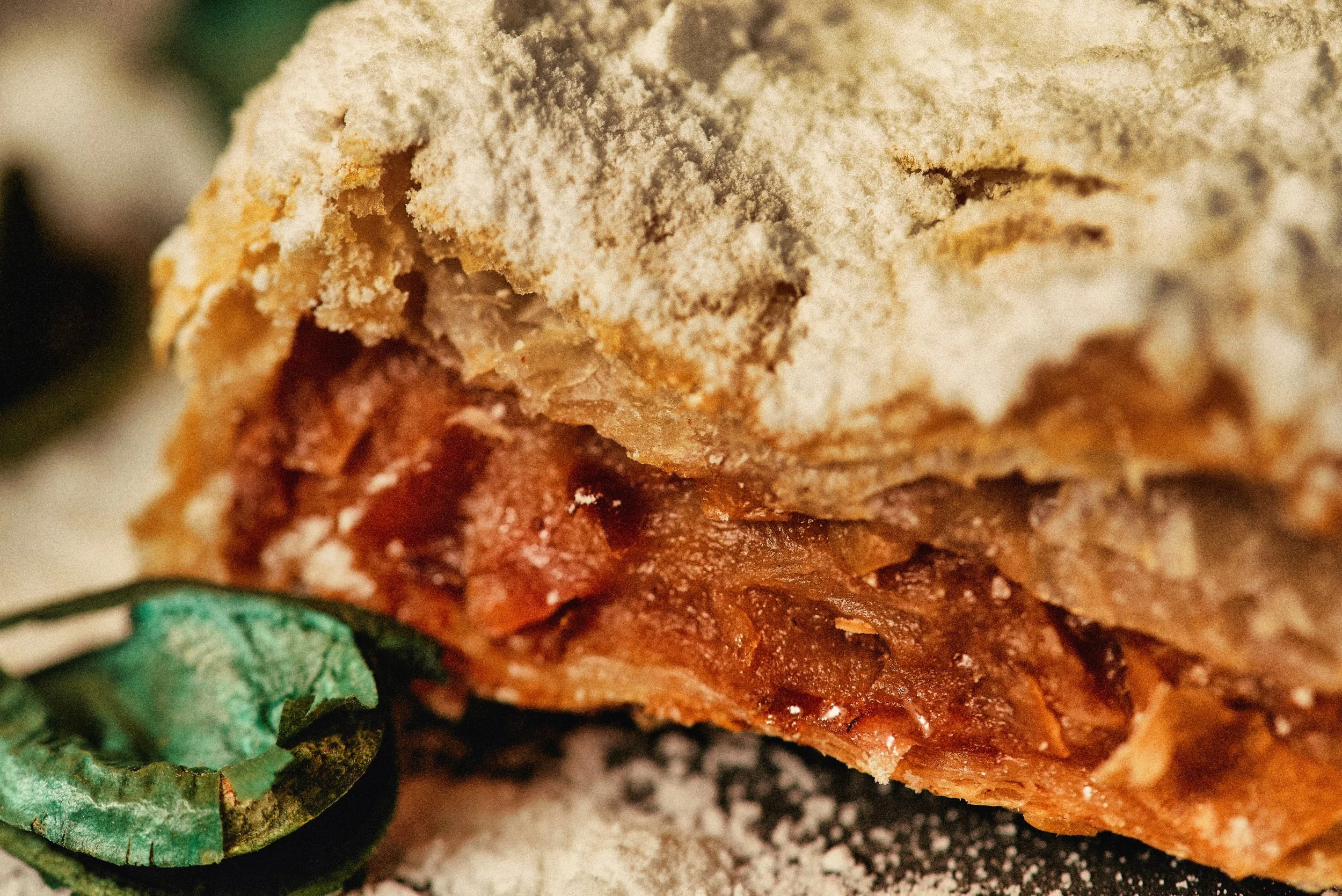 Close-up of a person seasoning a piece of cooked meat with specks of black pepper, surrounded by fresh green herbs.