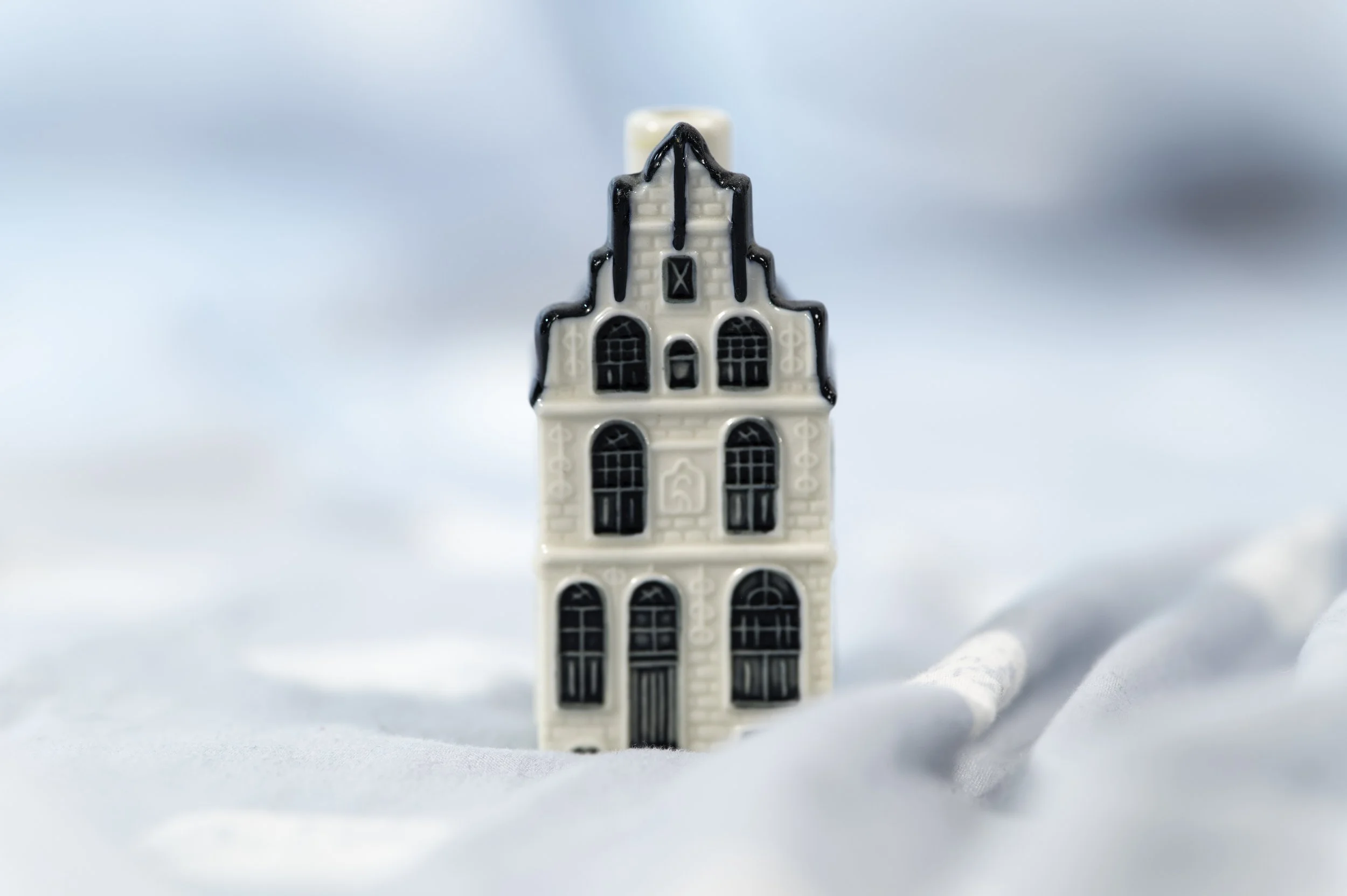 Close-up of a small architectural model of a multi-story building with detailed windows and doorways, set against a blurred light blue background.