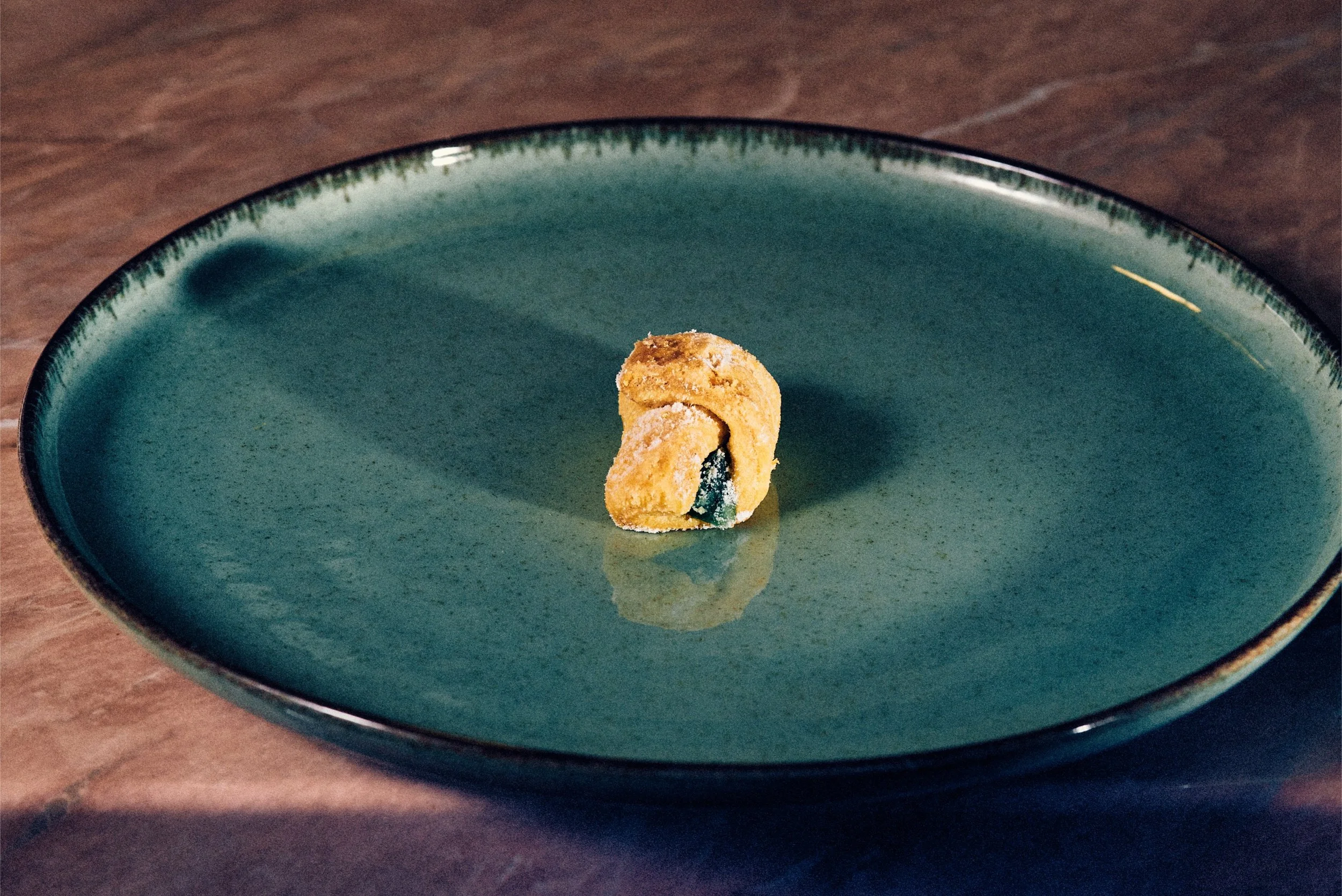 A single piece of fried food, possibly a chicken nugget or a fried cheese ball, sitting on a teal ceramic plate.