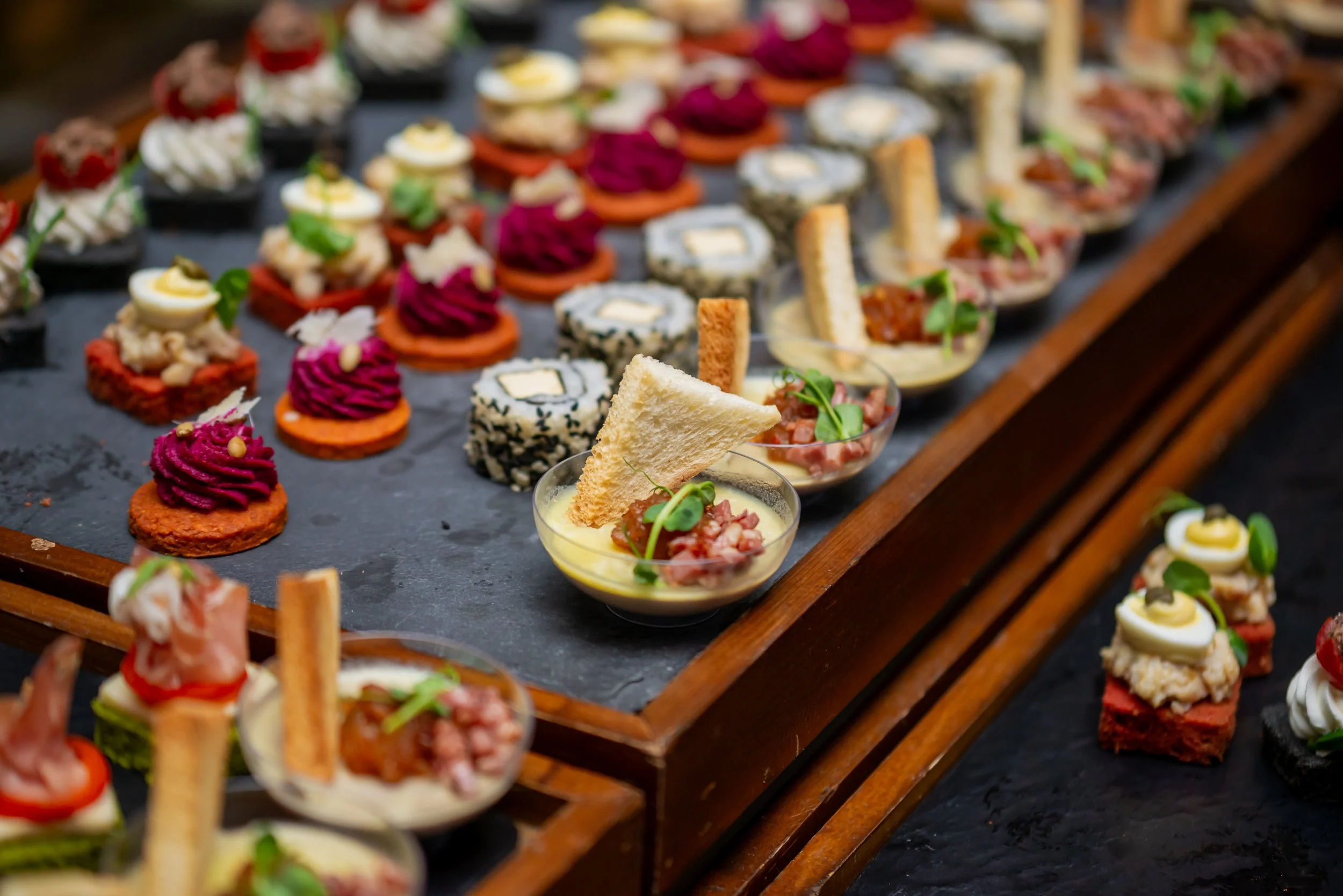Assorted bite-sized appetizers and canapés arranged on a black slate serving board.