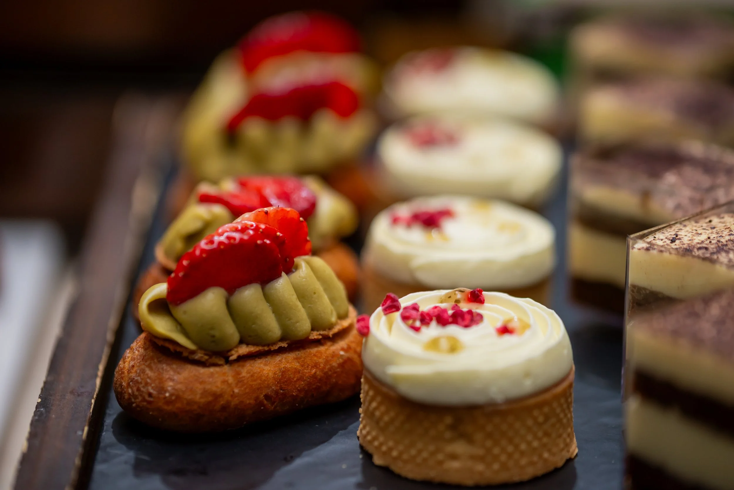 Assorted cupcakes with various toppings including strawberries, red sprinkles, and frosting in a display case.