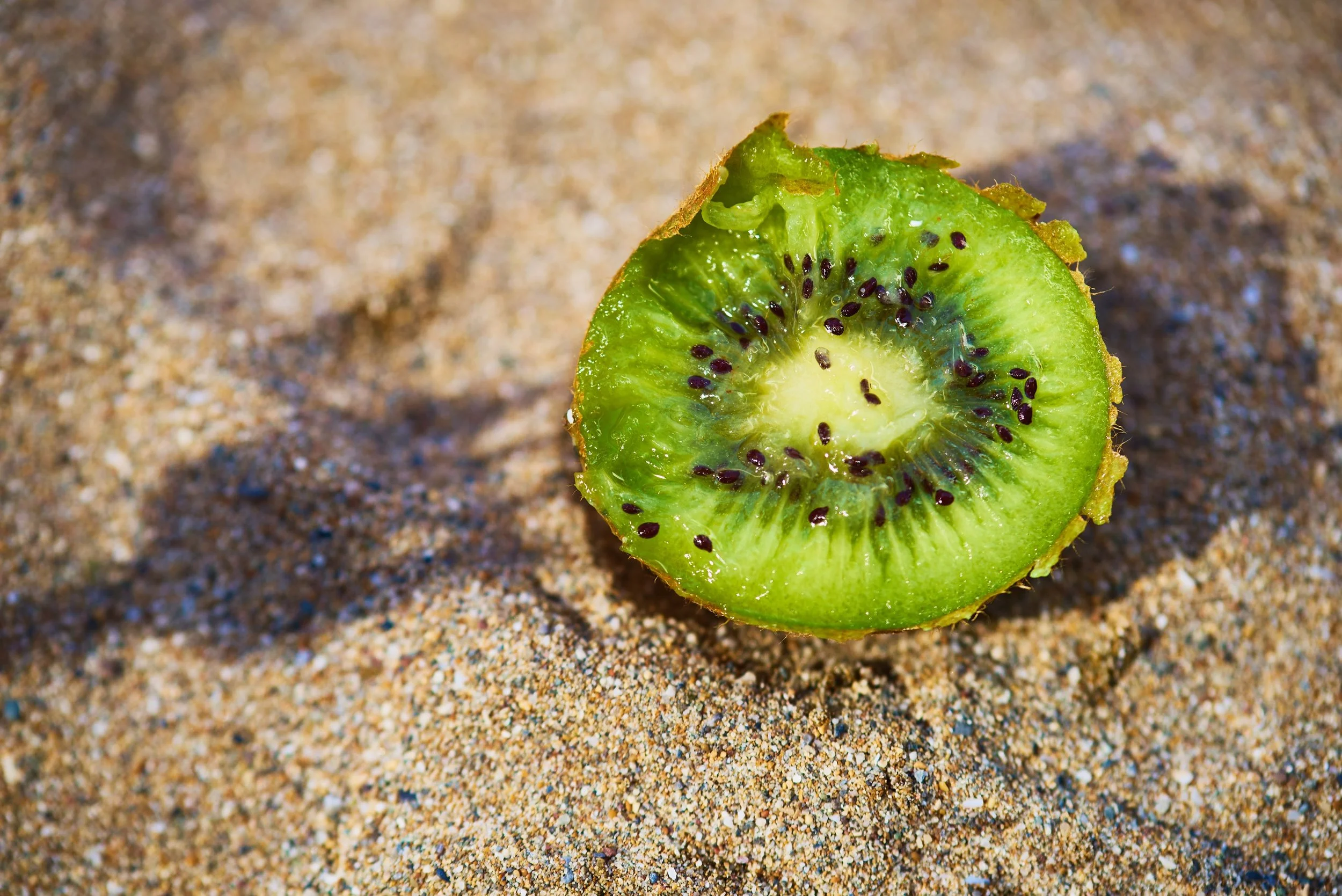 Close-up of a halved kiwi fruit on sandy ground.