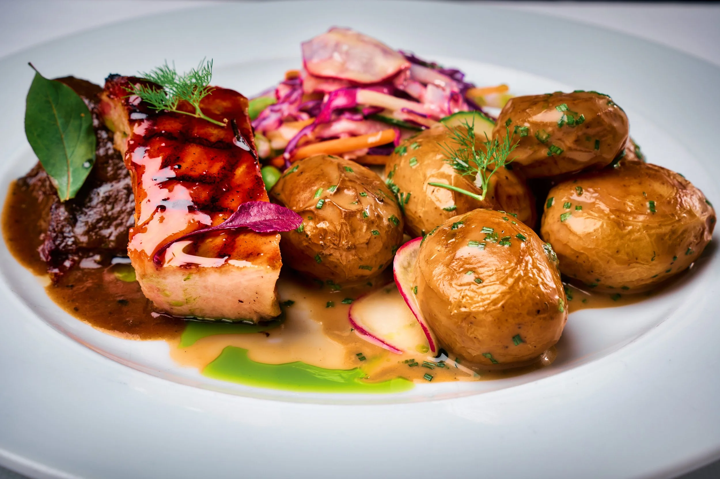 A plated dish featuring meatloaf topped with gravy, served with stuffing and vegetables, and garnished with herbs.