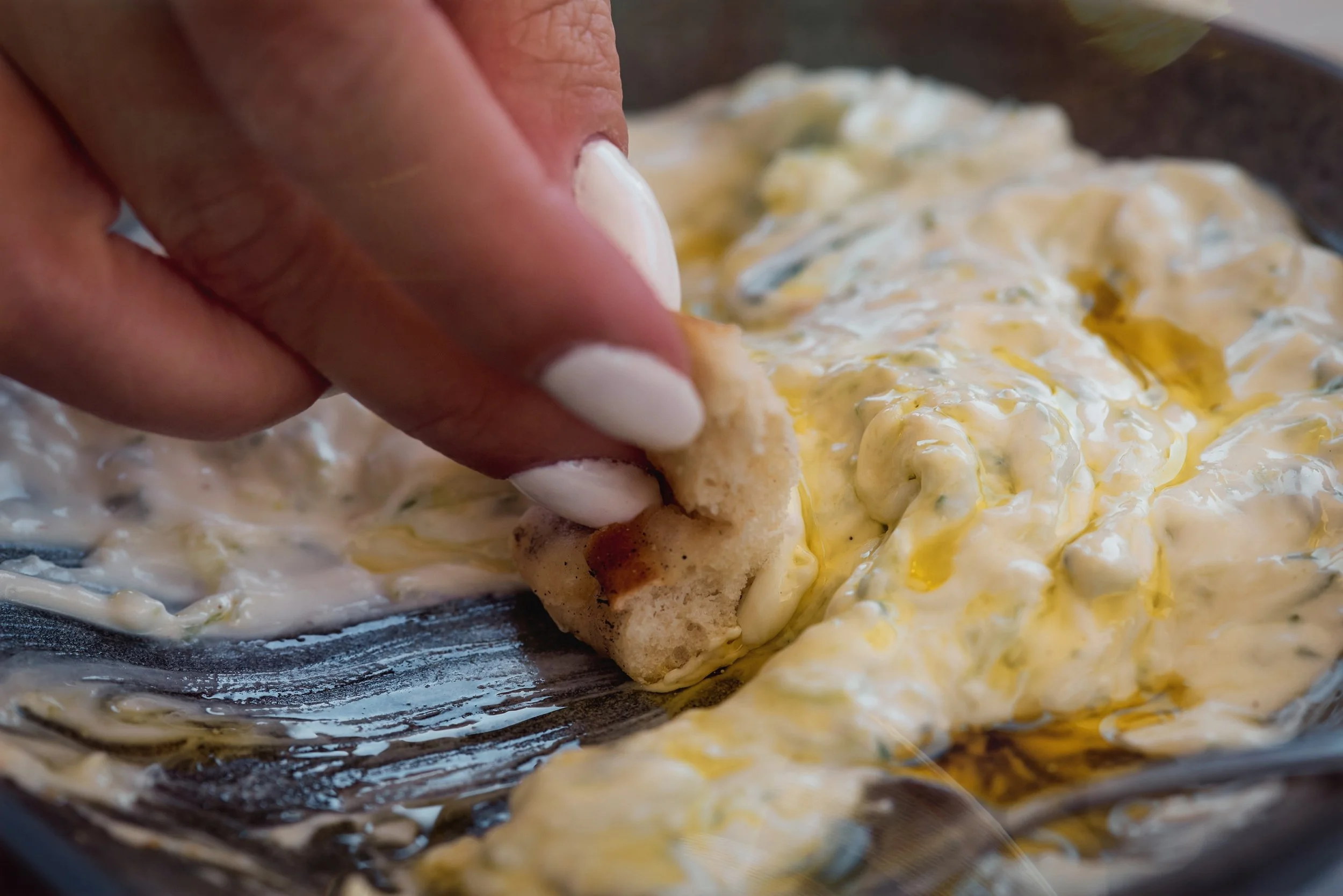 Close-up of a hand holding a piece of bread with creamy egg salad on top, being prepared in a skillet or pan.