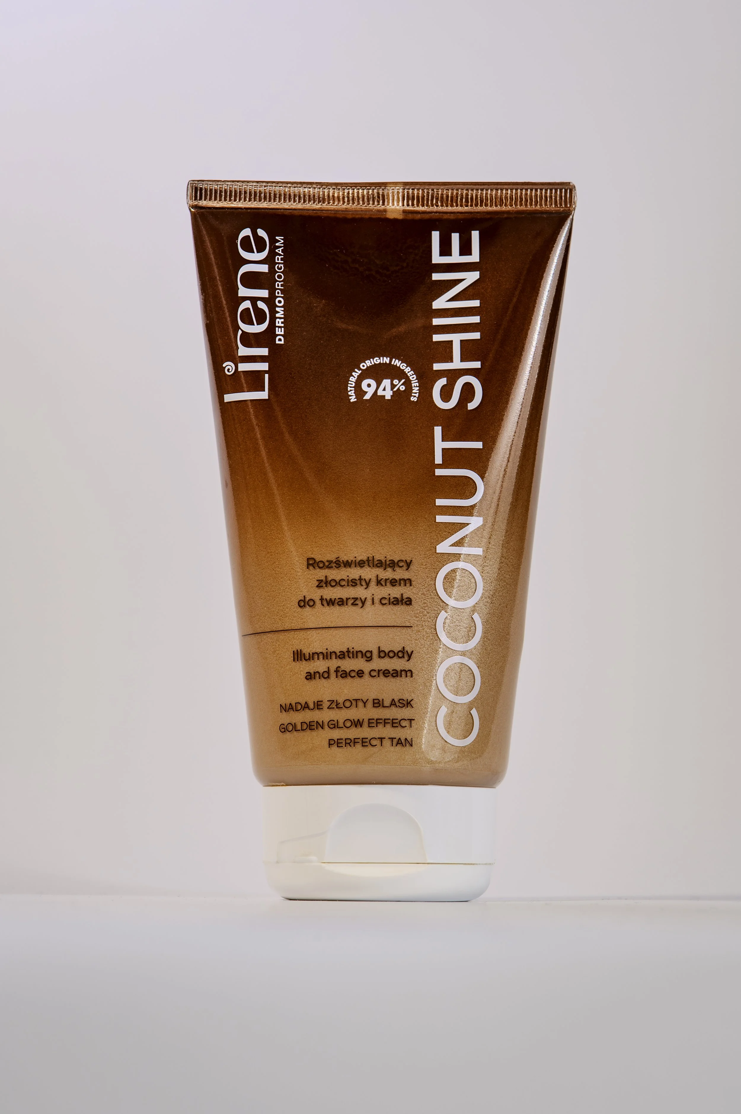 A tube of CC Cream, a cosmetic product, with the top part visible. The tube is a bronze or copper color with white text in English and Polish, mentioning its features like illuminating body and face cream, with 94% natural ingredients, and providing 