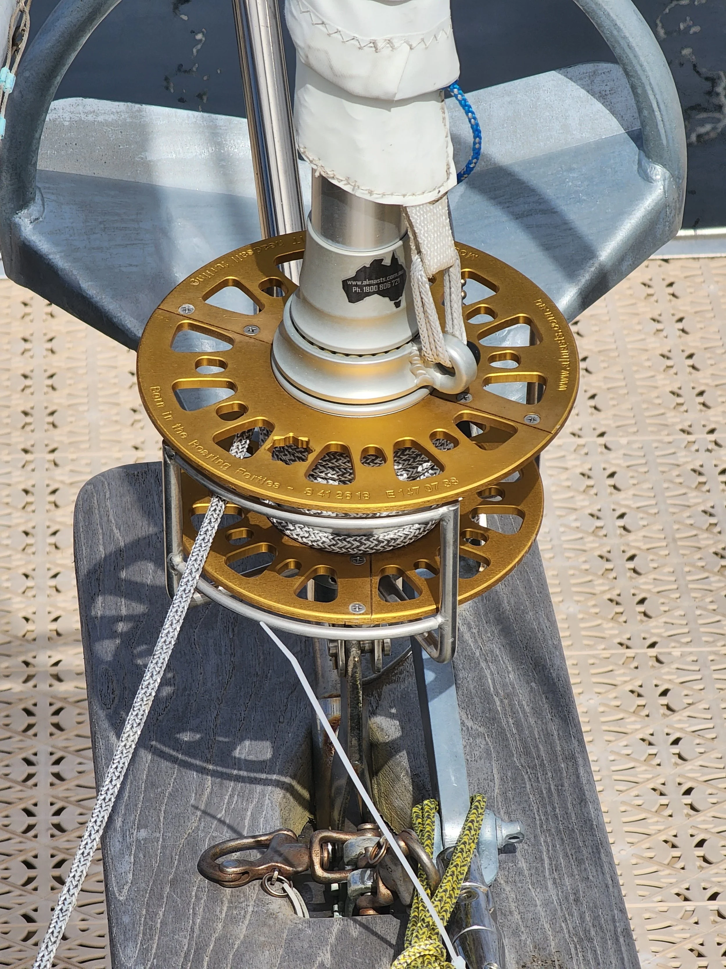 Close-up view of a boat's bow with a gold-colored anchor support plate, ropes, and a wooden bow pulpit, on a metal dock surface.